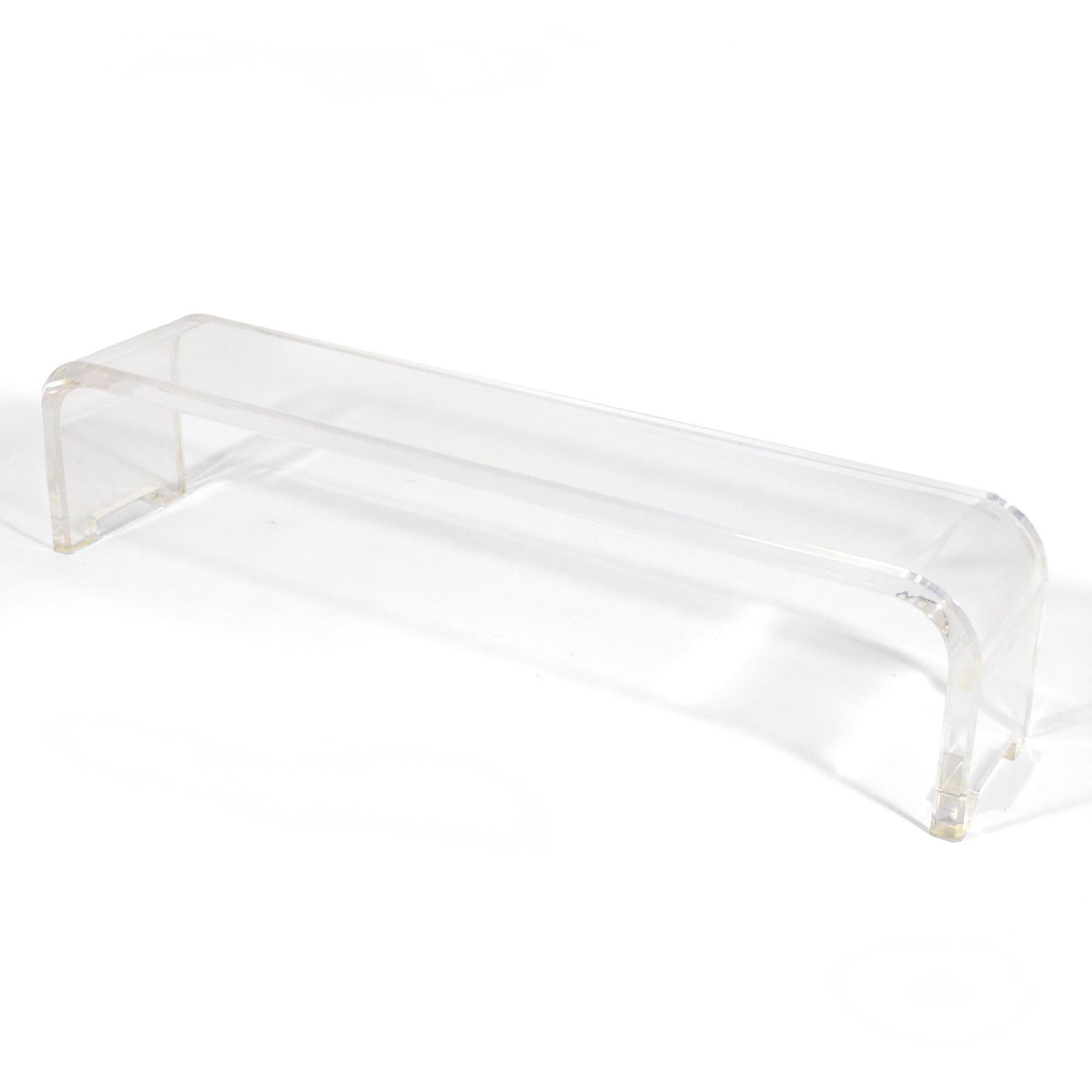 This large, dramatic bench is formed of one solid piece of lucite with waterfall edges and nicely detailed feet. The thick lucite gives it substantial heft belied by the light, transparent quality of the clear acrylic.

16.25”h X 71.5”w X14”d