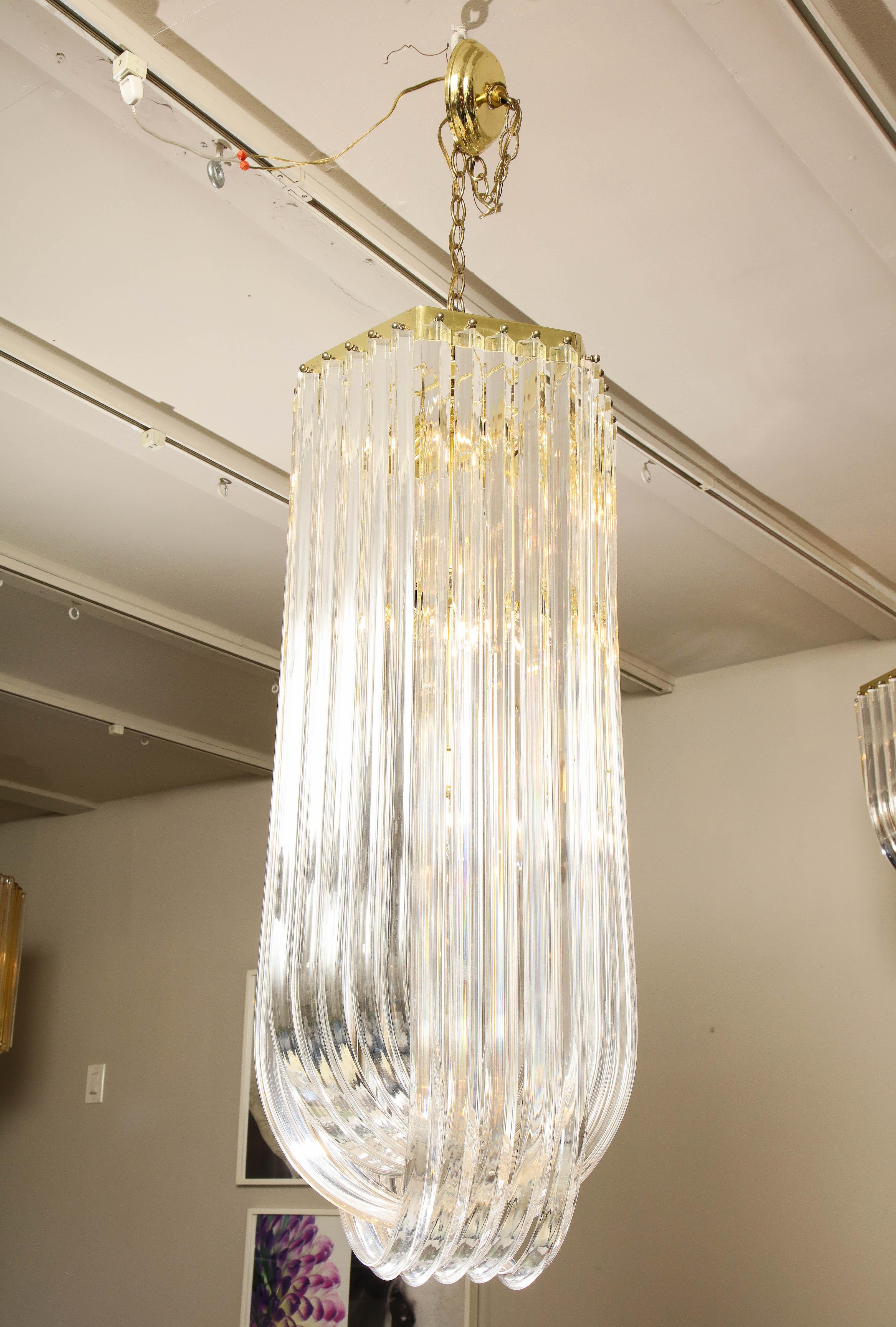 Long midcentury curved Lucite ribbon chandelier in brass finish. 15 candelabra (E12) sockets. Some aging on brass frame and scratches on acrylic pieces.