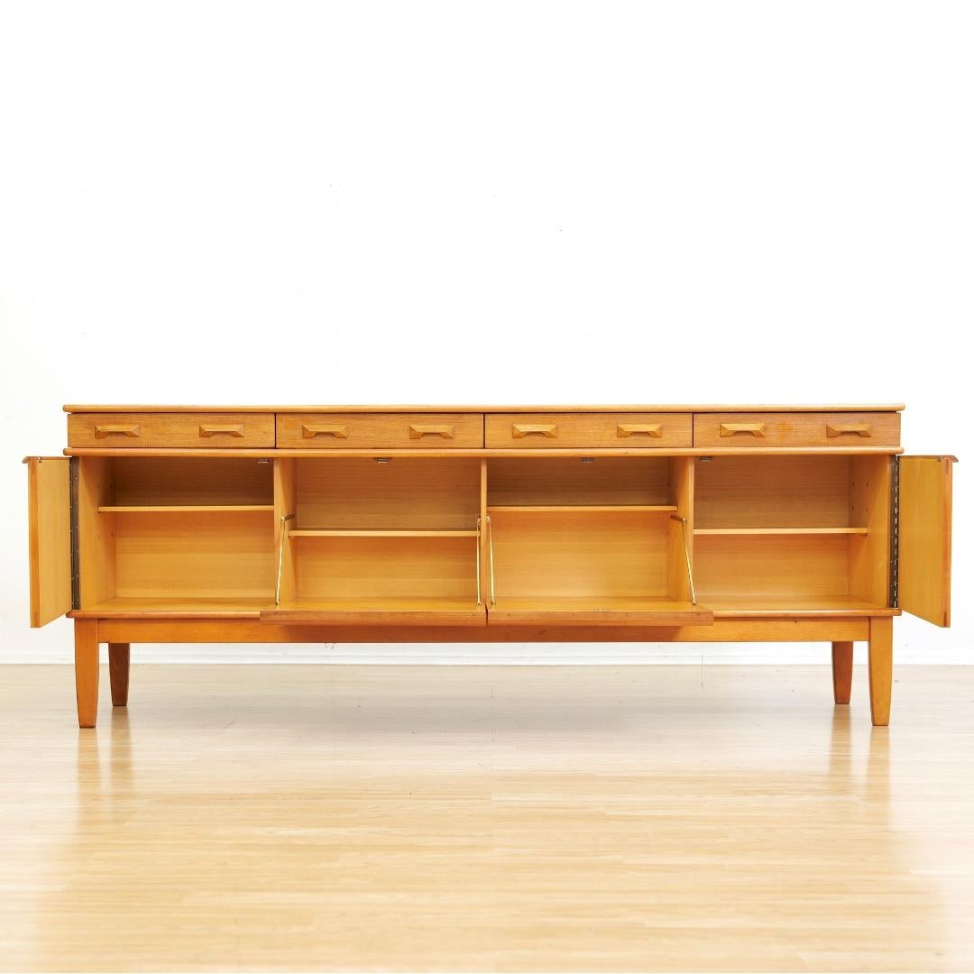 Credenza della metà del secolo scorso progettata e prodotta in Inghilterra negli anni '60. Questa credenza di grande impatto vanta un'ampia capacità di contenimento grazie ai quattro cassetti e alle quattro ante con ripiani. Le ante anteriori hanno