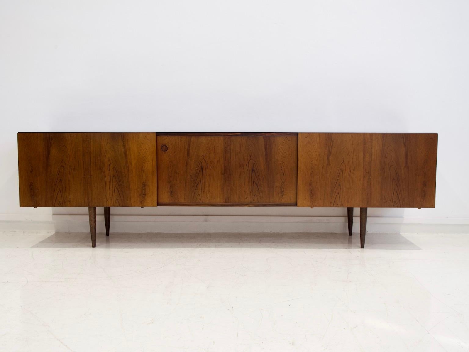 Low sideboard designed by Ib Kofod-Larsen and manufactured at Faarup Møbelfabrik in the 1960s. Veneered with hardwood, front with sliding doors, behind which are shelves and felt-covered trays. Later mounted tapered legs.