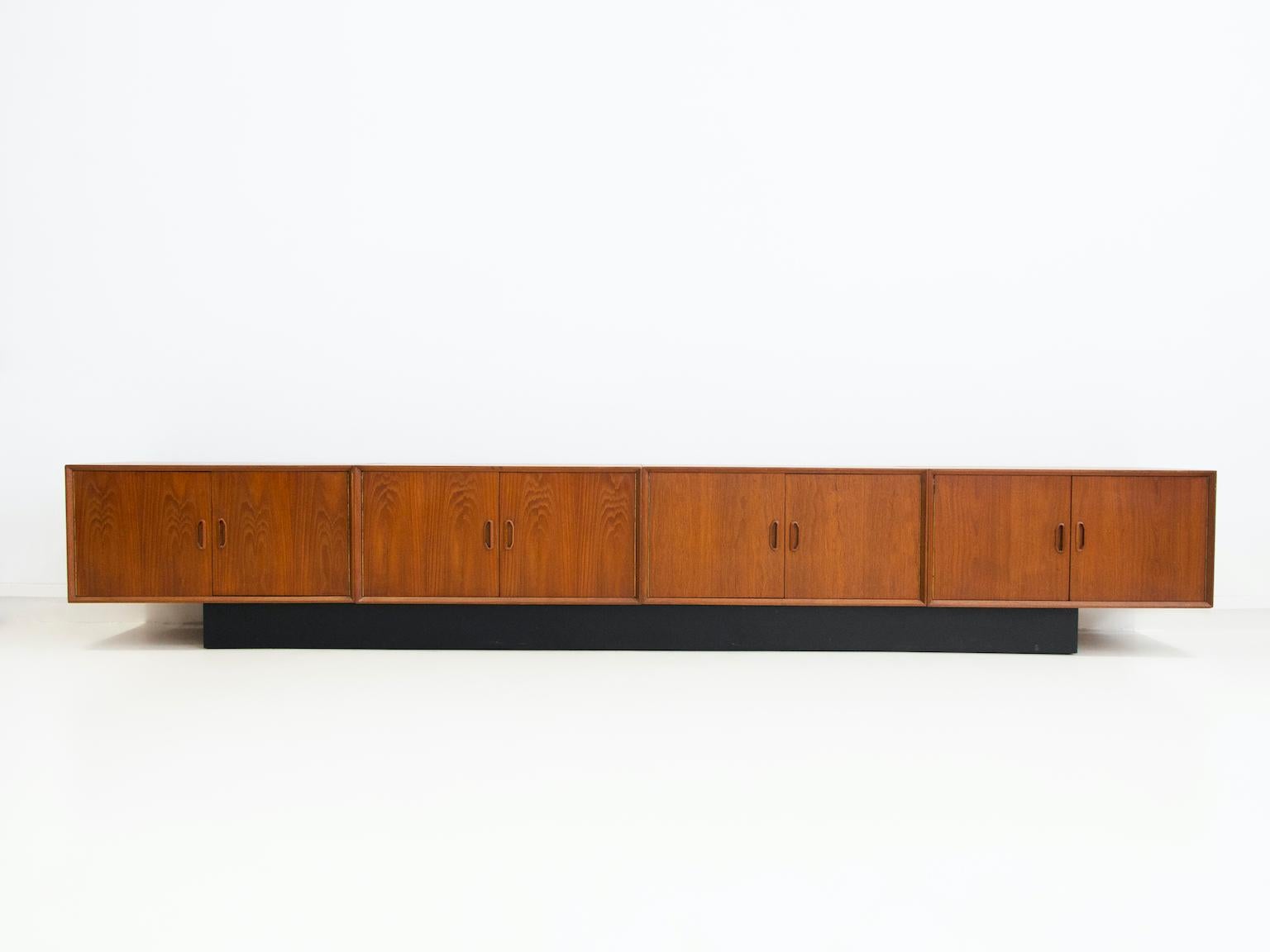 Long Scandinavian made teak sideboard of four parts with later rectangular black painted base. Each part with two doors, behind which there is storage place. Only one with a shelf inside. Back wall with a cut hole to store and facilitate plugging in