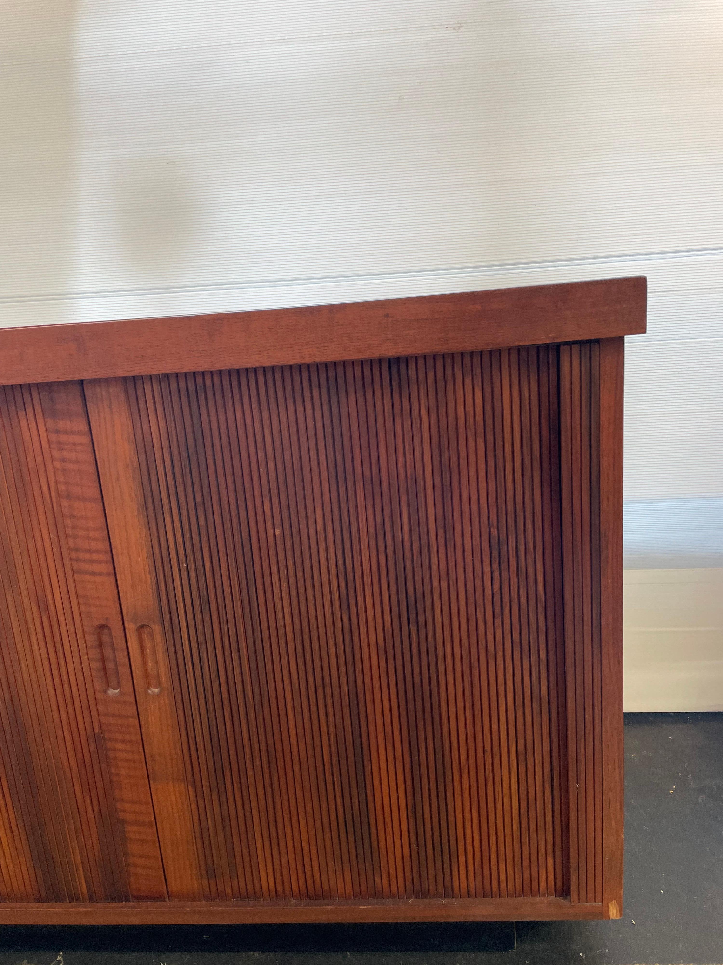 Vintage Mid-Century Modern credenza designed by Milo Baughman for Glenn of California in the United States c. 1950s. Comprised of walnut wood, this credenza has 2 sets of tambour doors with recessed pulls that reveal a compartment divided by a