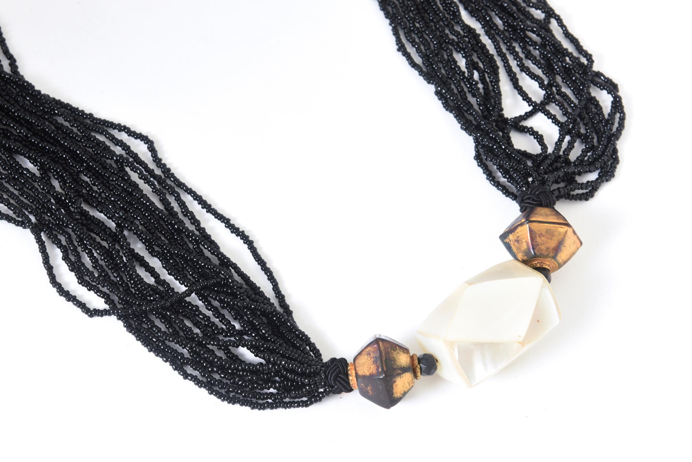 Vintage 18-strand black glass bead necklace featuring a large geometric bead with mother-of-pearl sections between two black faceted beads with a tarnished brass-tone bead. No clasp; cord knot. Age wear.