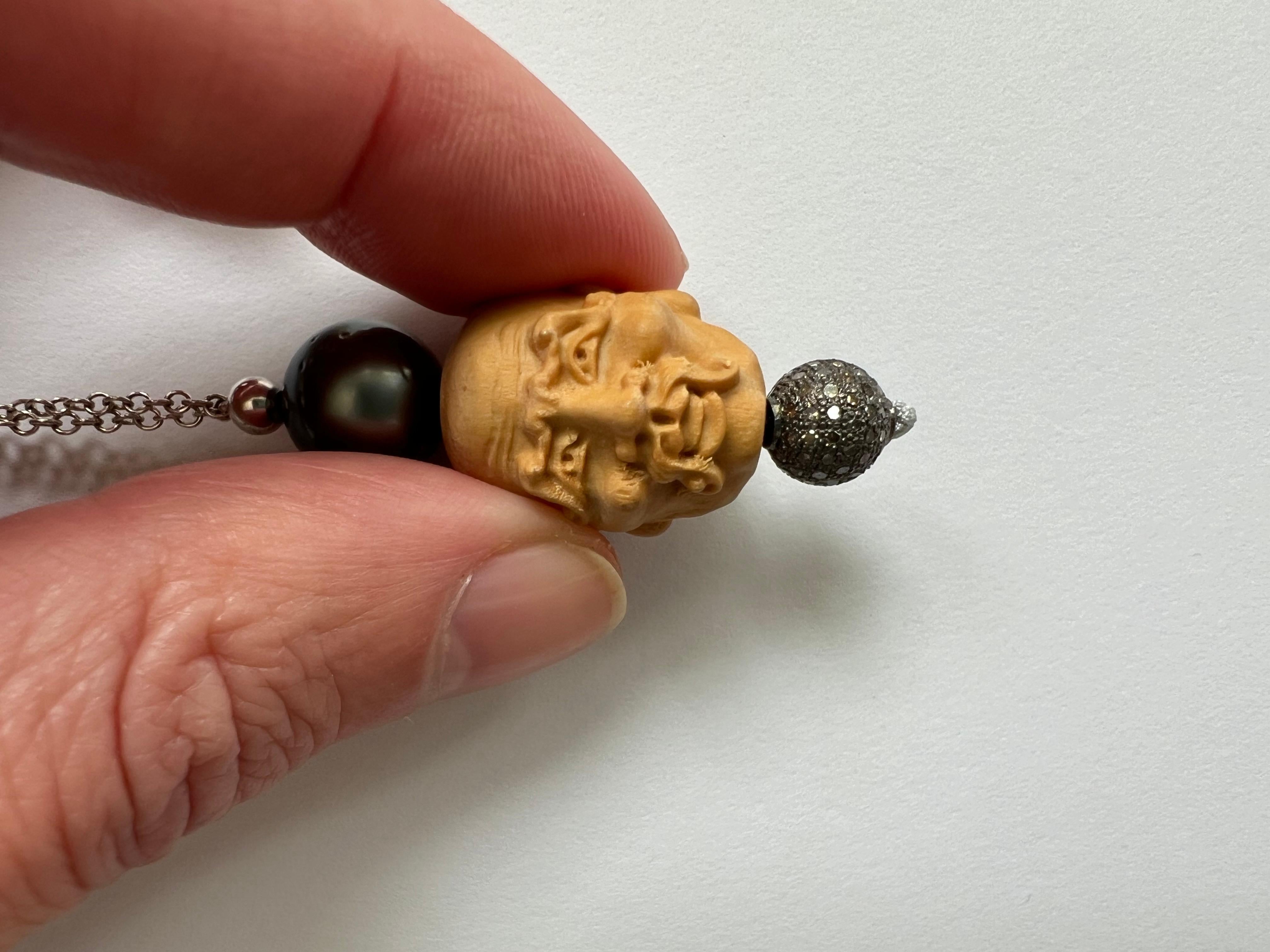 Una collana lunga davvero unica. La catena è in argento 925 e ha una lunghezza totale di 44 cm, compreso il ciondolo di 4 cm. 
Il ciondolo è costituito da una perla di Tahiti grigia di 11 mm di diametro, da un volto di Buddha in legno intagliato a