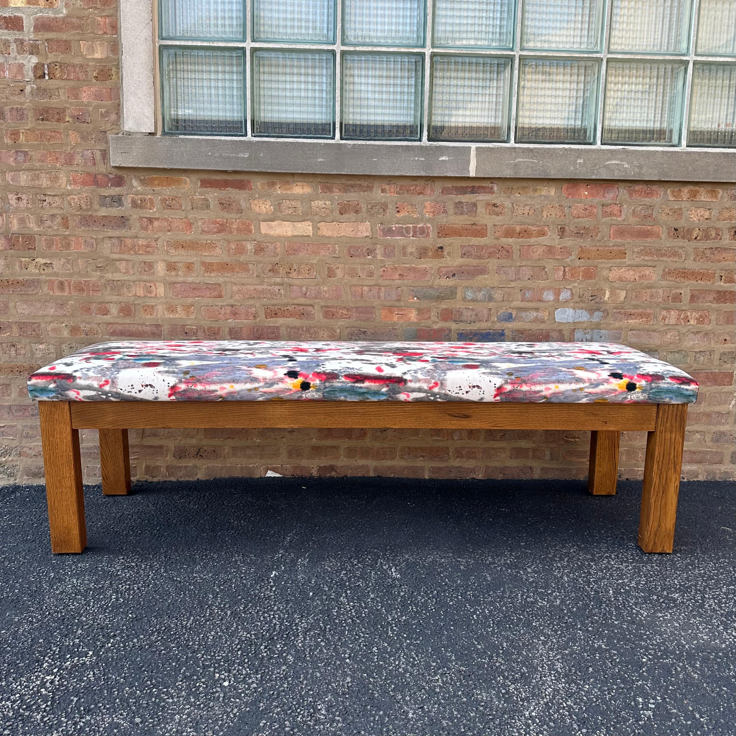 This long and beautiful bench is constructed from solid oak. The bench has been upholstered in a Holly Hunt velvet fabric that evokes an abstract watercolor art piece. The substantial size of the bench, combined with the gorgeous splash of colors,