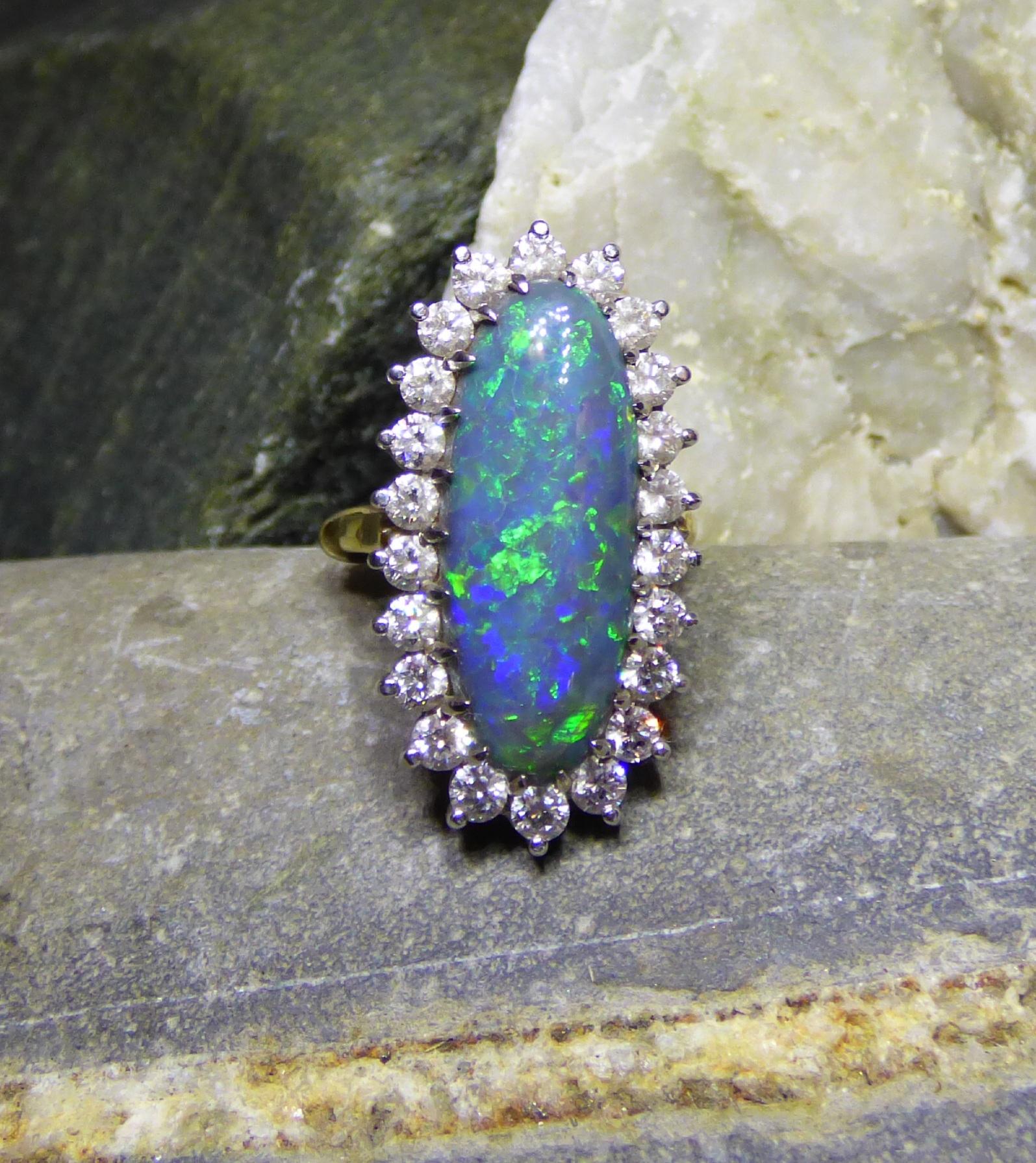 A colourful natural black Opal  (11cts) is surrounded by 22 Diamonds (1.32cts). The total size of the cluster is 25X10mm in a handmade 18K yellow and white gold ring.  The ring is hallmarked by the Dublin Assay Office.
This magnificent ring fills