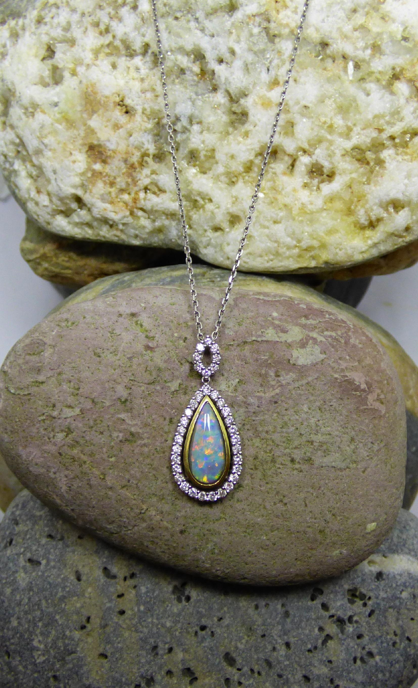 A brilliantly colourful pear shaped Opal is set in a handmade pendant. 
The Opal is 14X5mm (1.62ct.) surrounded by Diamonds. The bale is also set with Diamonds ( total Diamond weight is  .83ct.) The 18K yellow and white gold pendant is hallmarked by