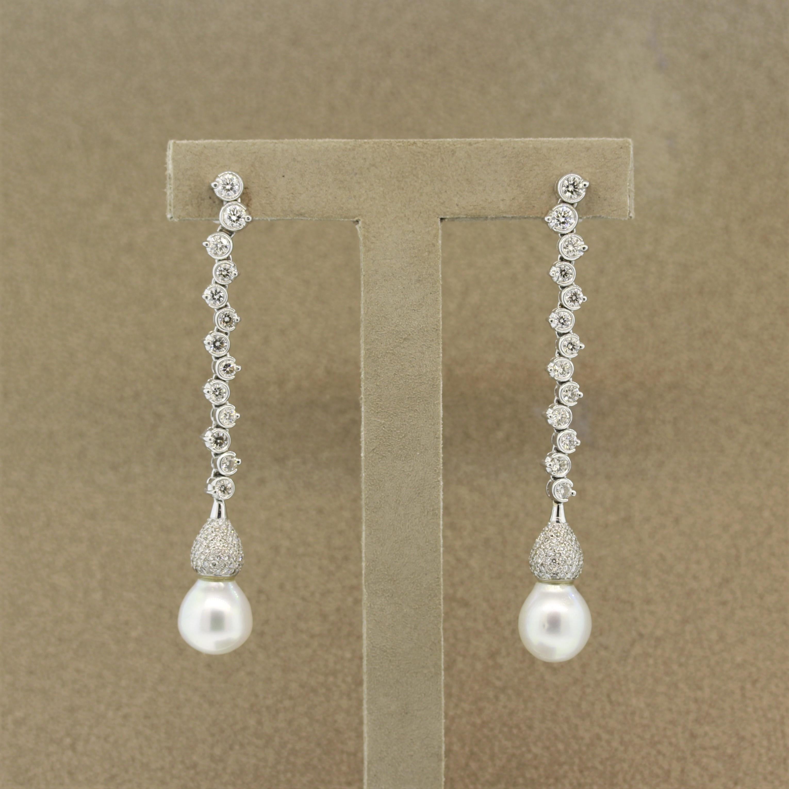 A long chic pair of diamond and pearl earrings. They feature 2 drop shaped white Akoya pearls with a soft pinkish green pistachio overtone that glows. Complementing the pearls are 4.00 carats of round brilliant cut diamonds which run along the