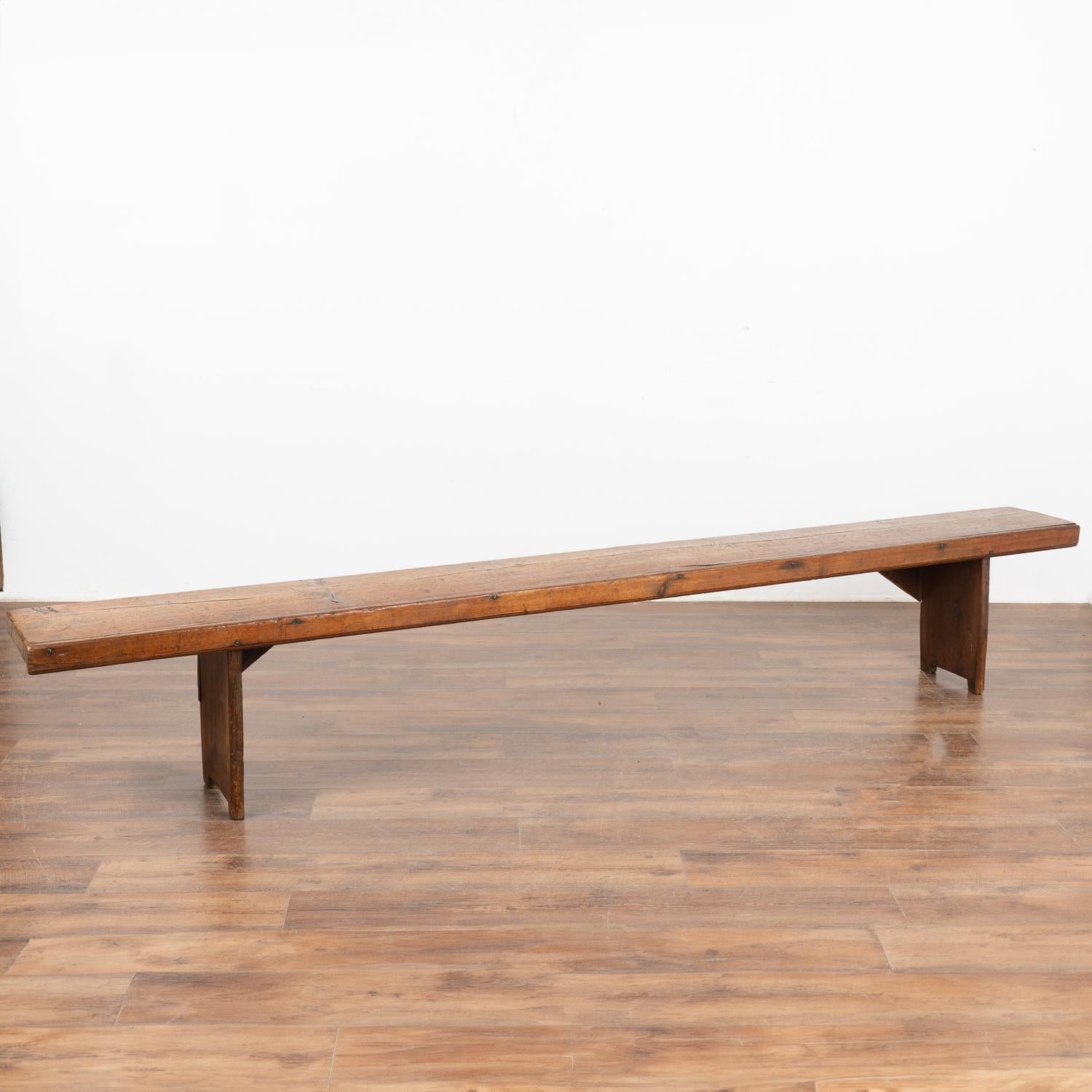 Rustic narrow 9' plank top bench with deep aged patina.
The top reveals generations of use with nicks, cracks, stains and scuffs which add character to the narrow bench.
Restored and waxed, this bench is strong, stable and ready for use. 
All