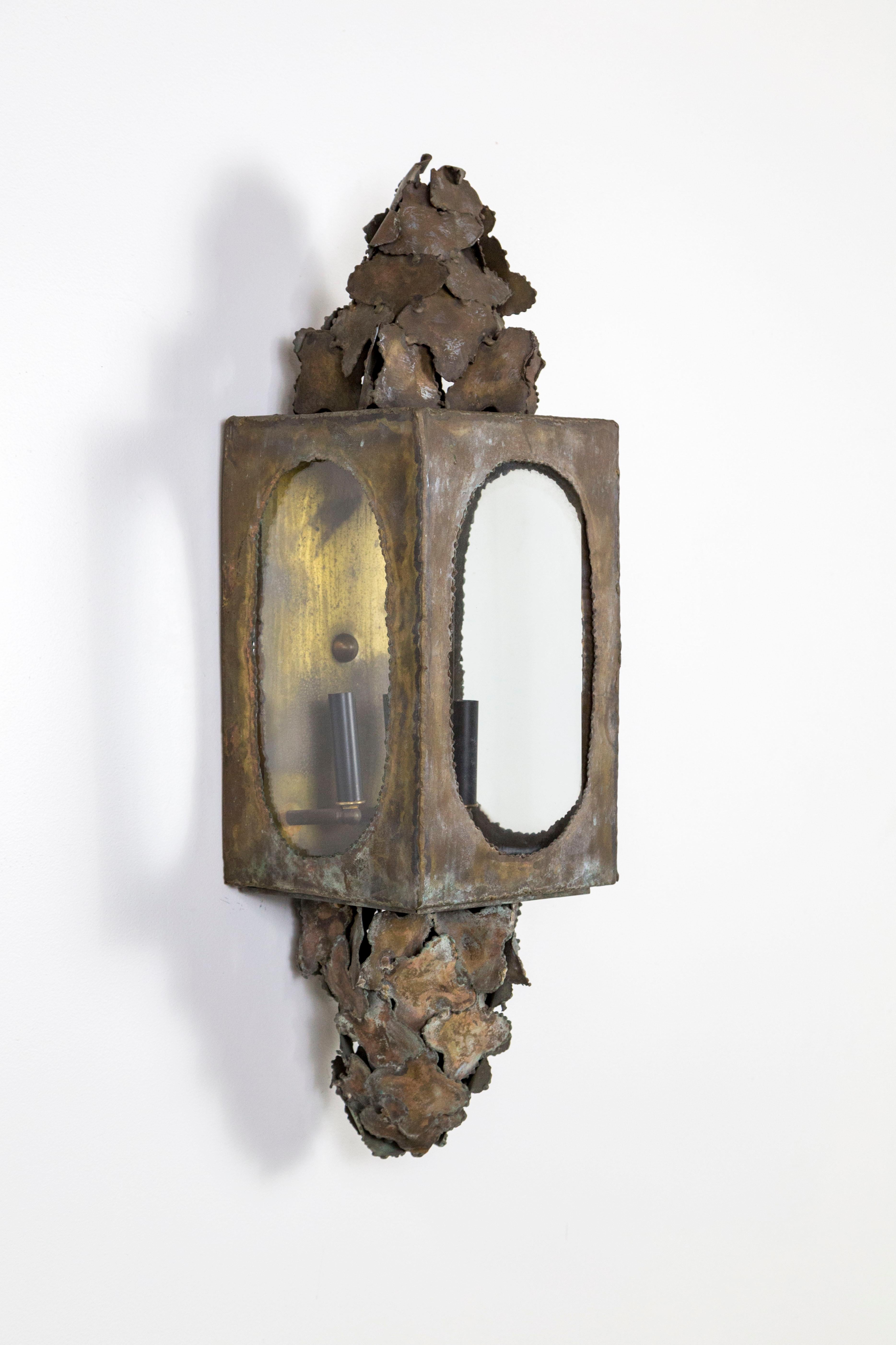 An incredible, large Brutalist sconce with beautiful, varied patina with a multi-dimensional look, and hand soldered, sculptural brass accents. Lantern-like style and long, rectangular shape; with three candelabra lights with black metal candle