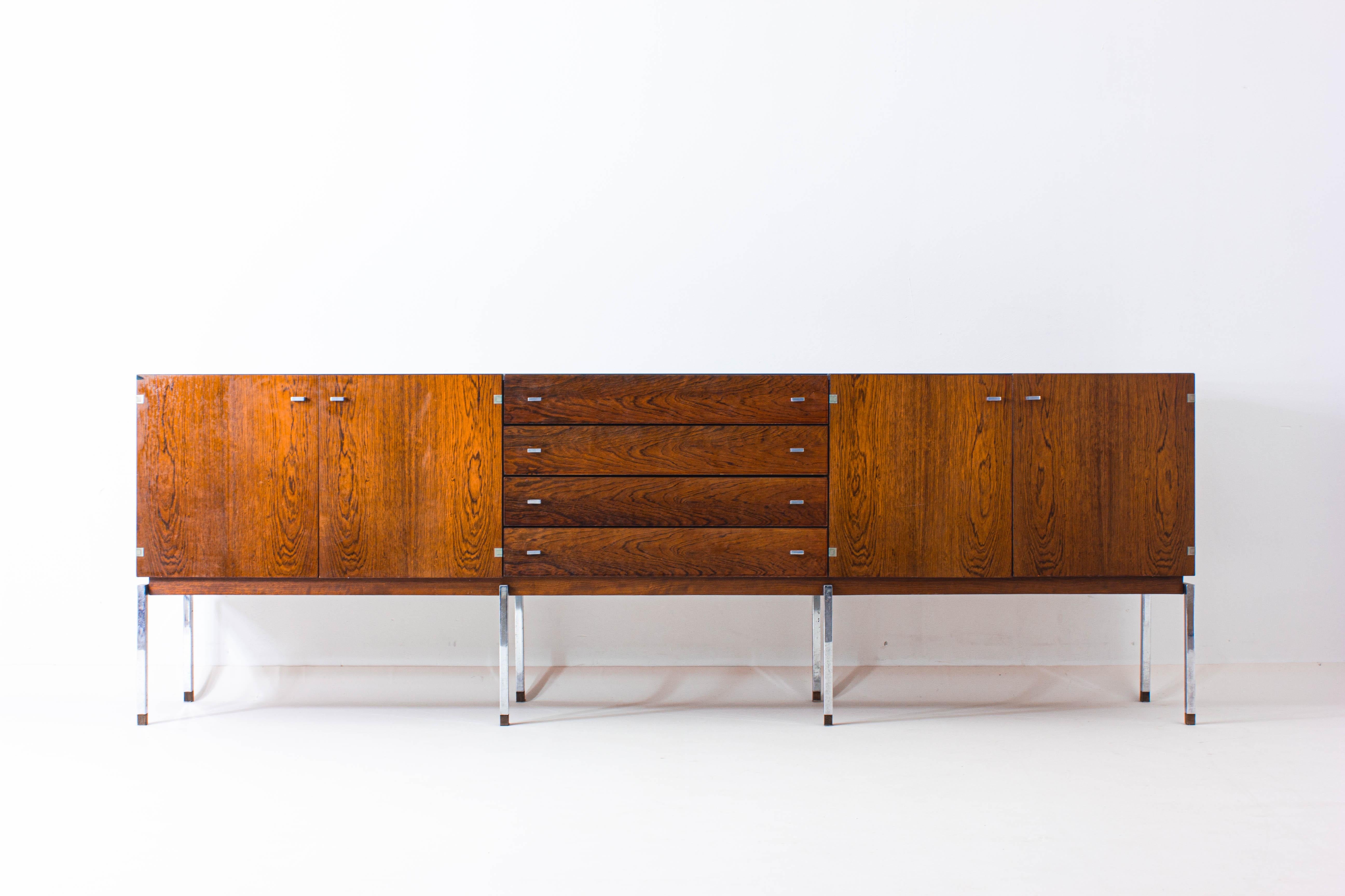 Extra long mid century sideboard made out of rosewood veneer and accentuated by chrome handles and legs. This sideboard brings refinement and elegance to any room thanks to its sleek lines and natural wooden colors.