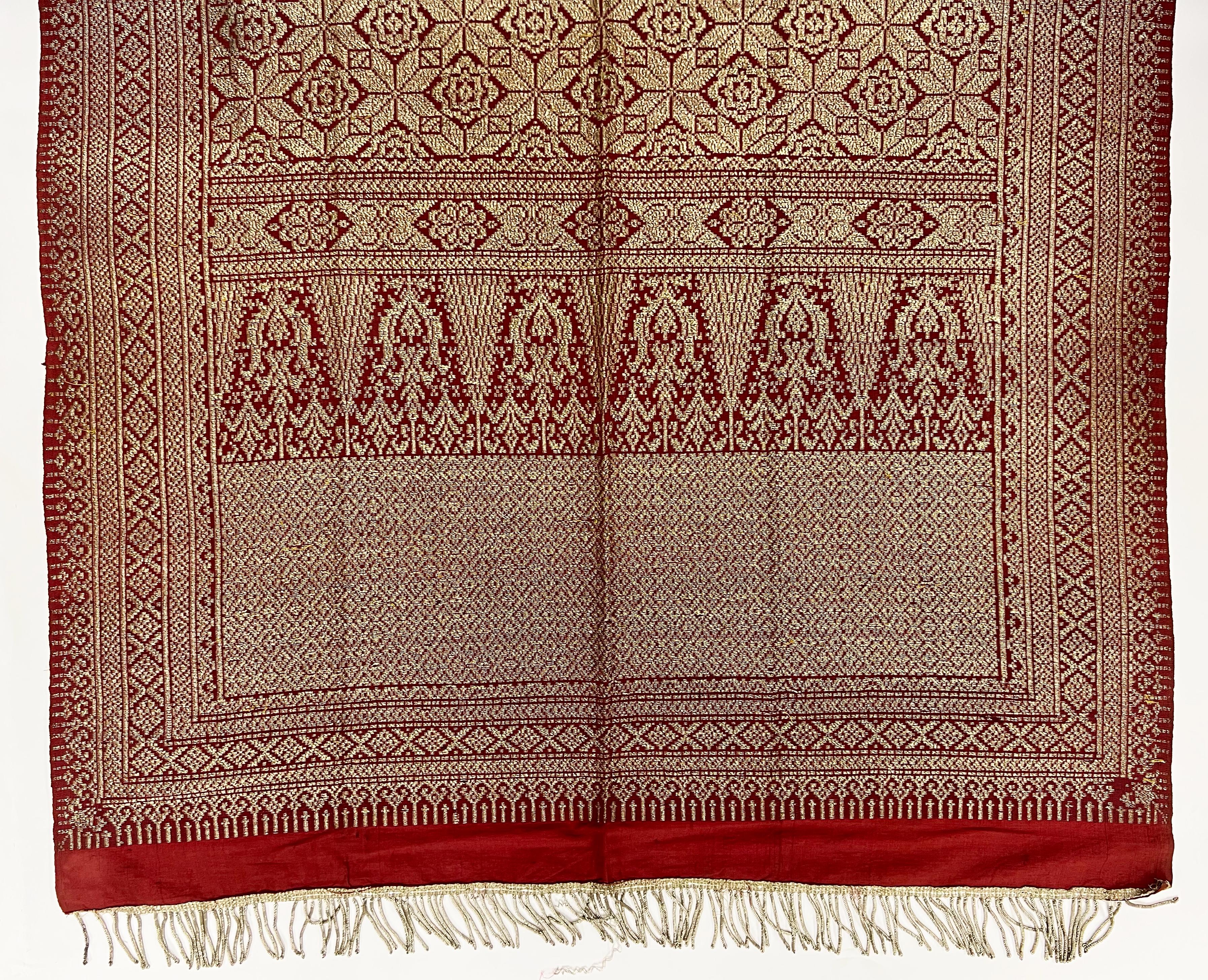 A fine silk and metal thread textile on a red background with various geometrical designs.
  