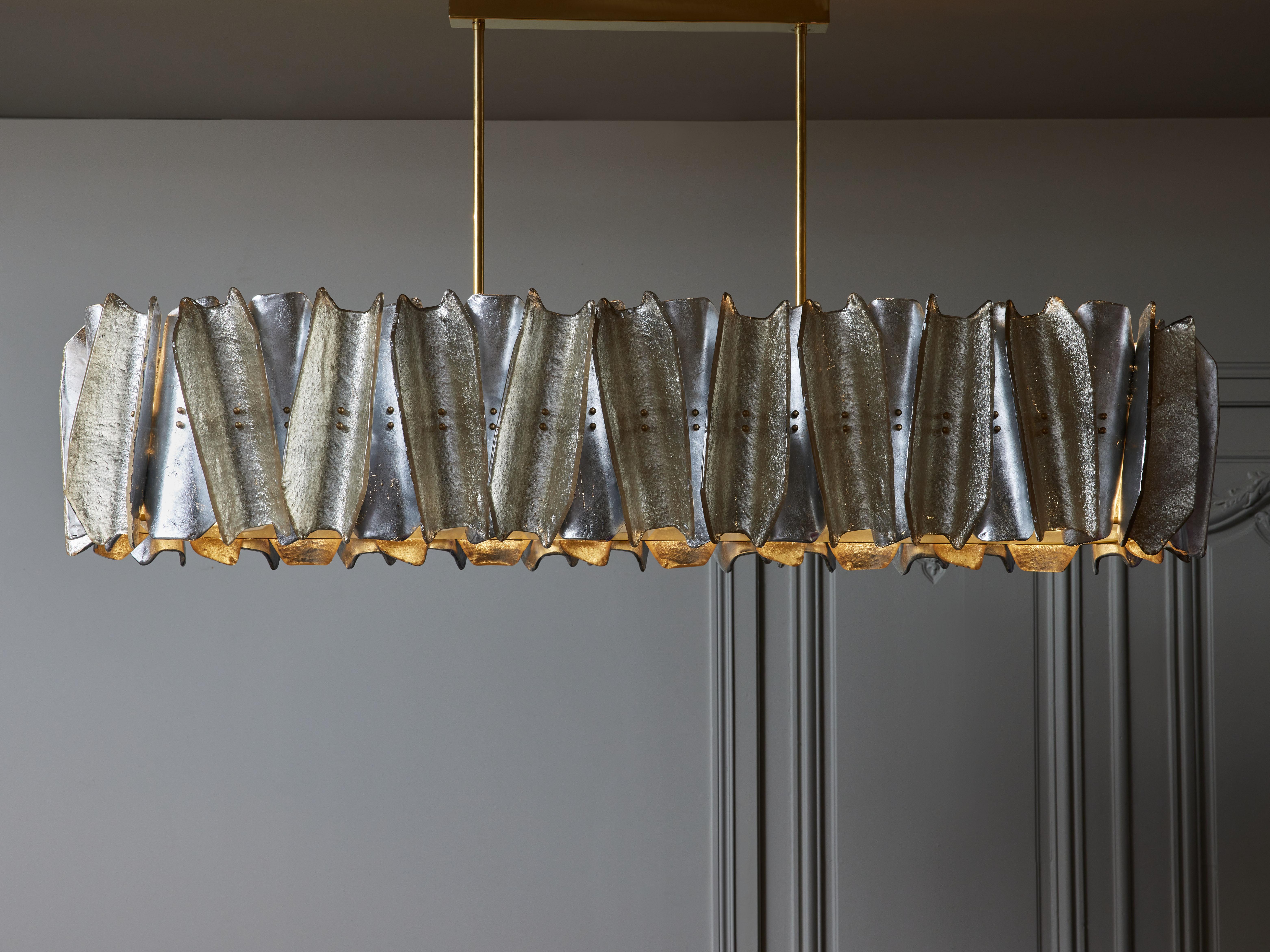 Elongated chandelier made of a brass structure, and Murano glass sheets bent and twisted, colored in silver and champagne. A large frosted glass plate covering the bottom of the chandelier and help to diffuse the light.