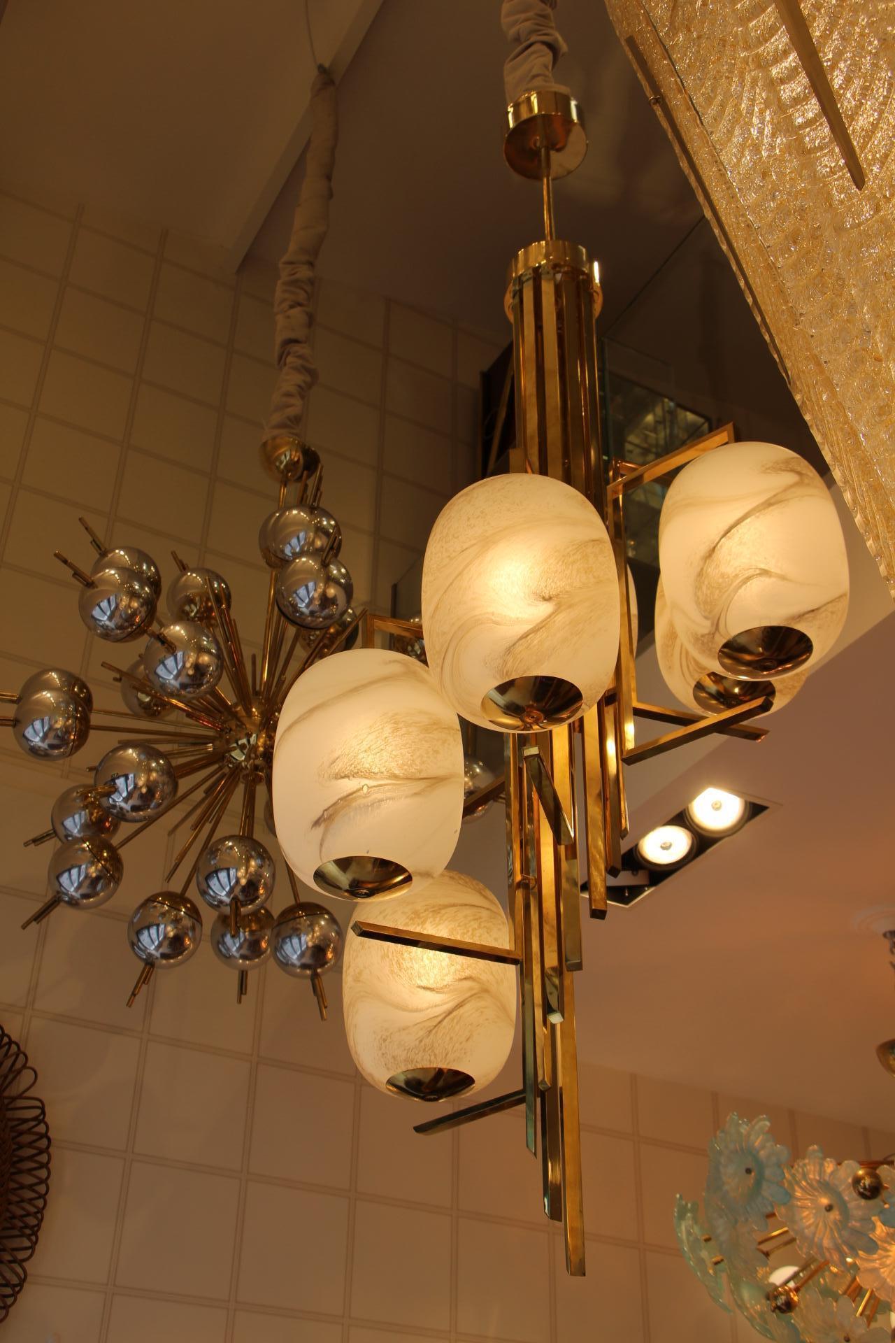 This spectacular chandelier features a main body made of several brass rods of different length and a series of 6 large globes in Murano glass looking like alabaster that turn and cascade like a spiral staircase.
It gives a warm and pleasant light
