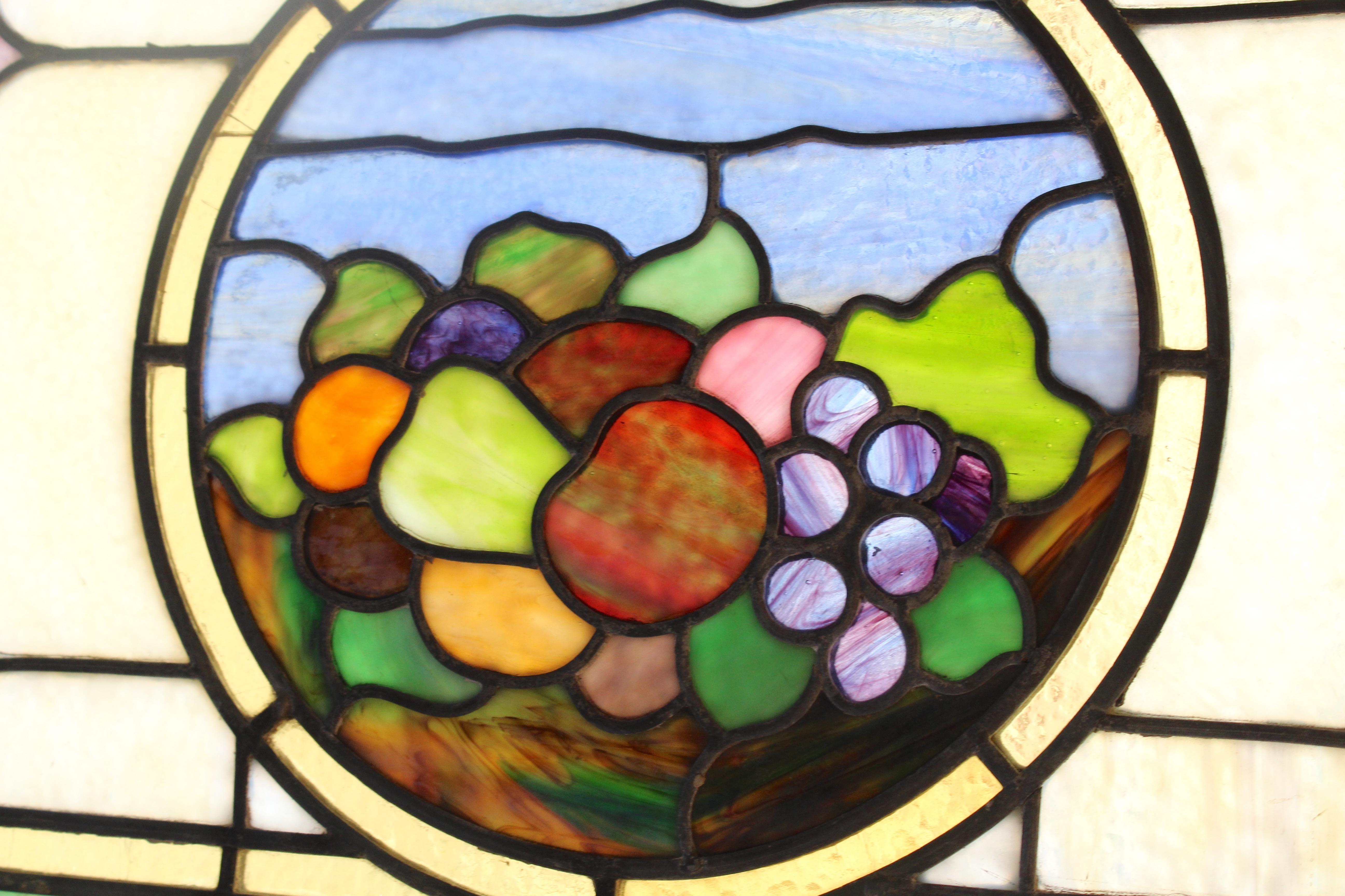 This window is over five feet wide, with a cornucopia centered. Wonderful coloring in each glass panel, and leaded designs throughout.
Currently housed in a wooden frame - the overall dimensions are for the stained glass and the frame.
Located in NY