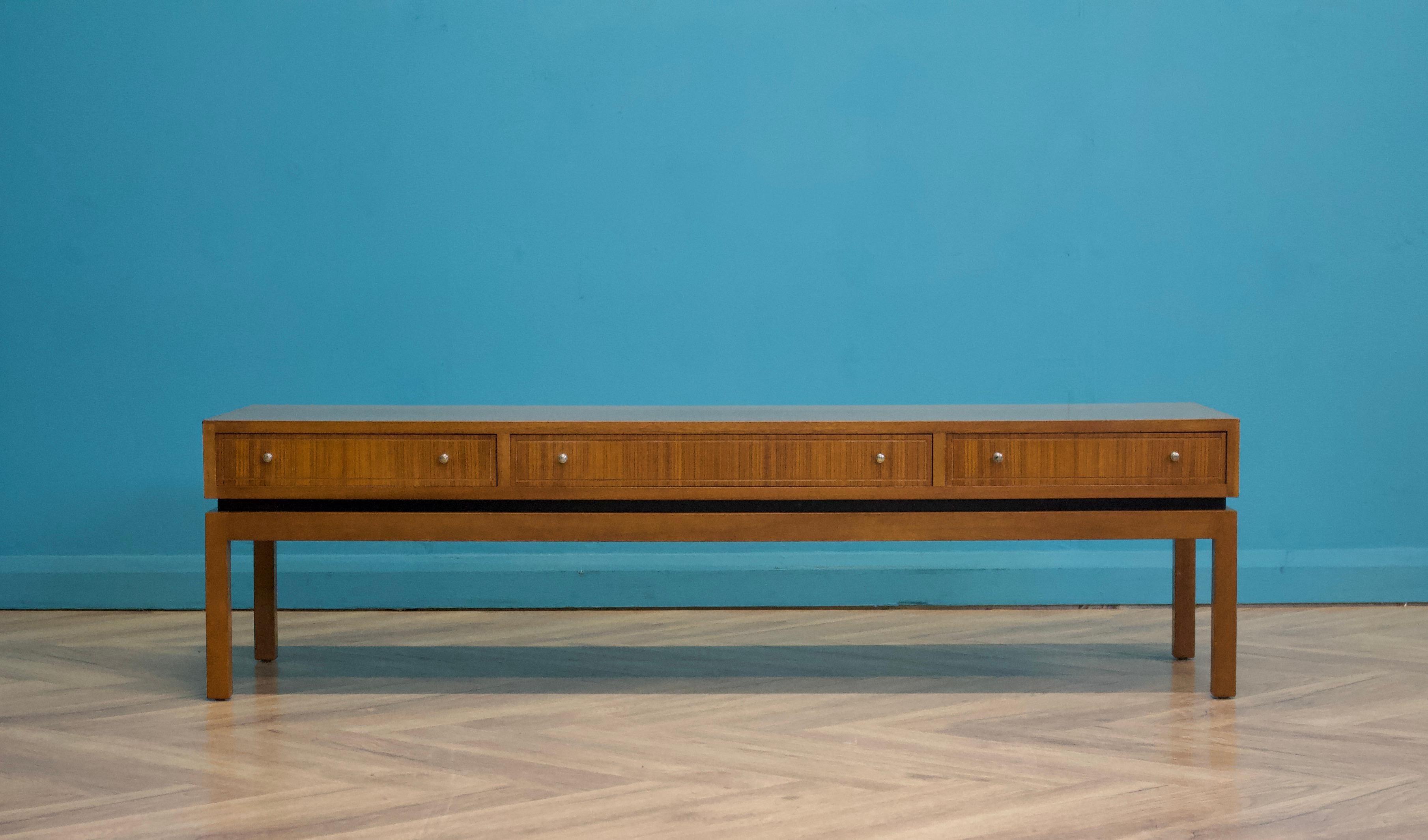 A mid century teak coffee table from Greaves and Thomas, circa 1960's
This coffee table has a long and low design, with three double sided drawers which are accessed from both sides


Featuring solid brass handles