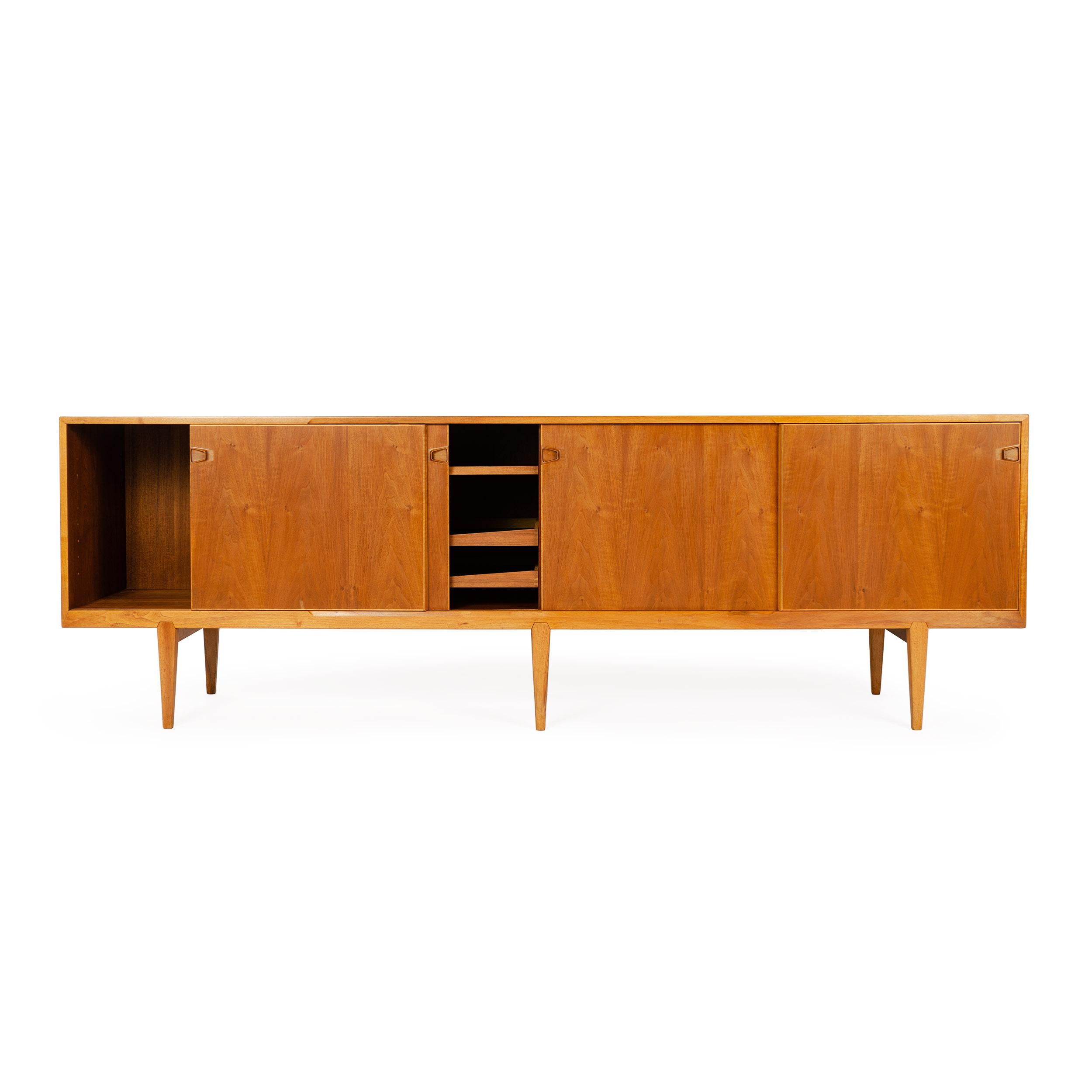 A walnut wood credenza designed by H. Rosengren Hansen featuring four sliding doors concealing shelving and drawers over six tapered legs. Made by Brande Møbelindustri in Denmark circa 1950s