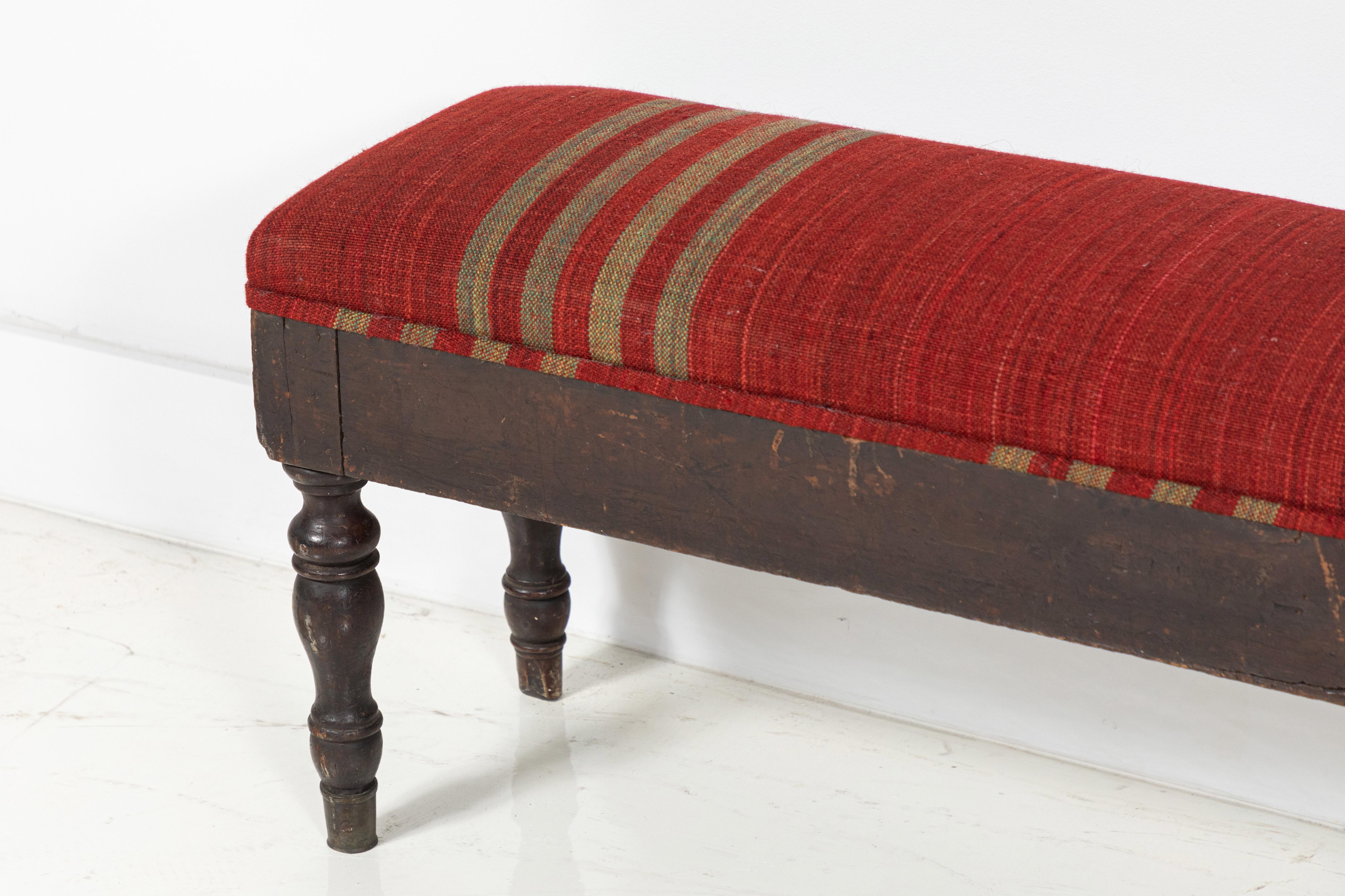 Long turned leg bench upholstered in red and gold textile from UK textile designer Susan Deliss.

 