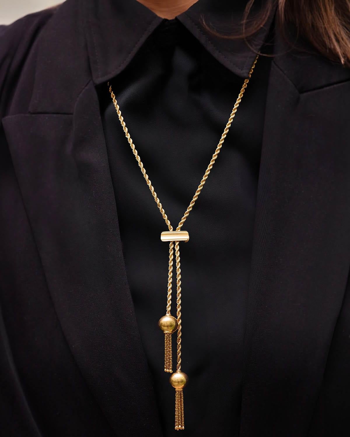 Ball tassels long necklace in 18 karat gold. This necklace features a twisted chain with two tassels hanging from the end. The chain is held in place by a slider attached to the chain, allowing the length to be adjusted and the asymmetry of the