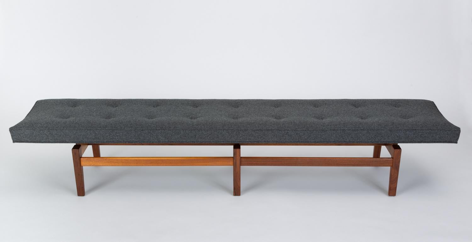 A rarely seen 8-foot version of Jens Risom’s upholstered bench. This example has been re-upholstered in Maharam’s Divina Melange 100% wool fabric in a charcoal gray. The walnut base has angled legs and broad support rails. Hidden spacers below the