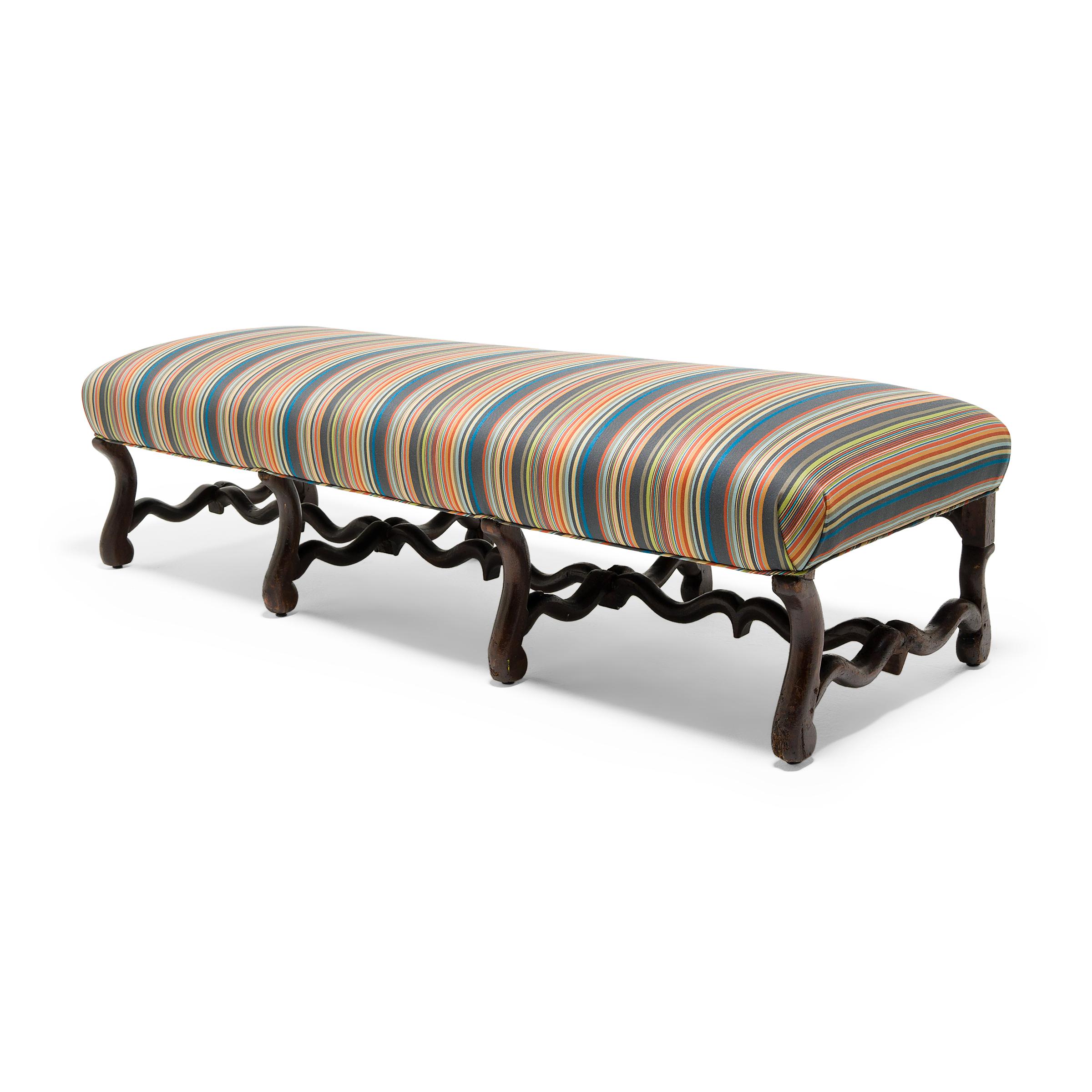 This gorgeous cushioned bench from the late 18th century is crafted in the Louis XIV style with an upholstered top and beautifully carved legs and stretchers. The walnut base is carved in a style known as os-de-mouton, or sheep's bone, a