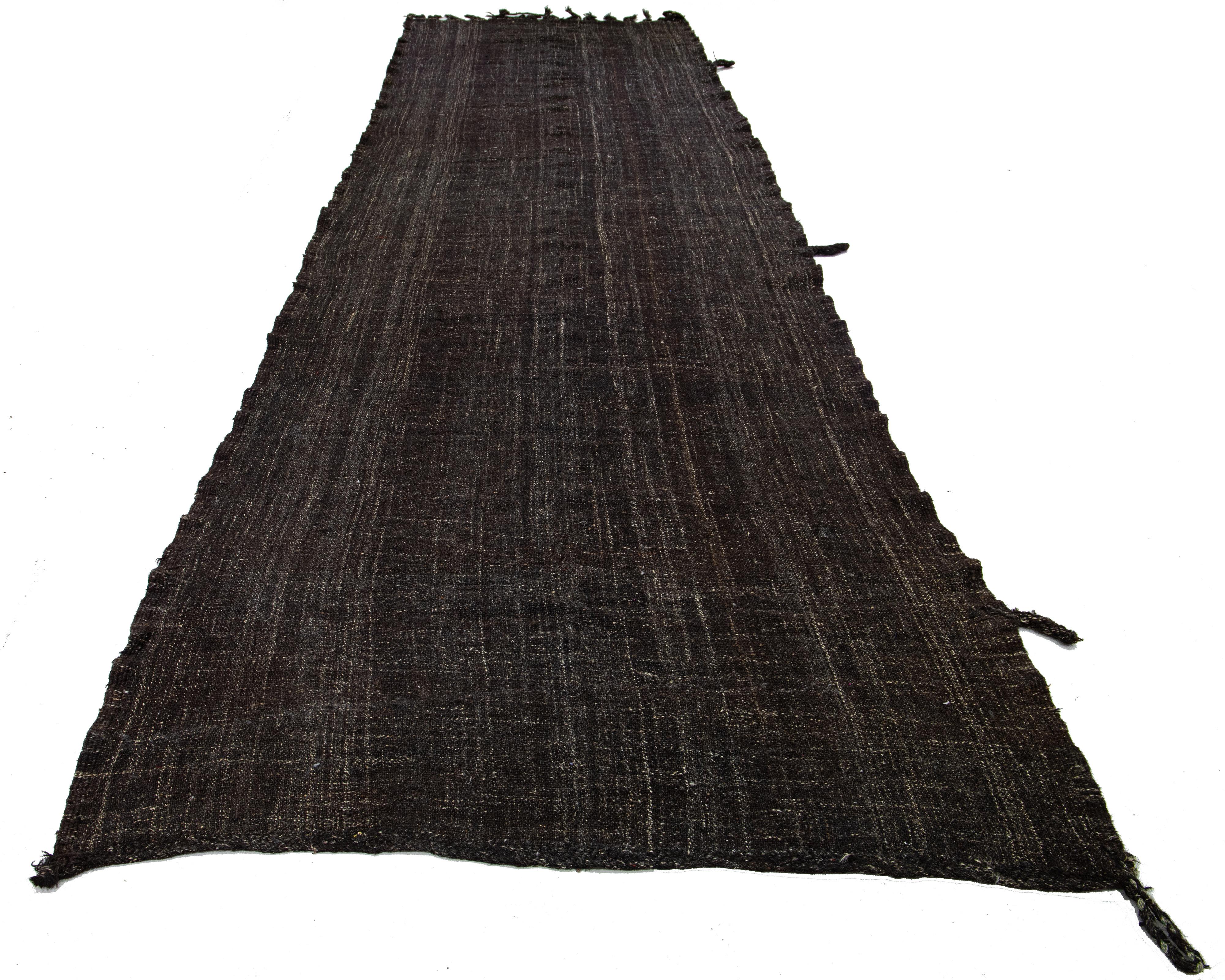 The Deco flatweave wool runner displays a striking dark brown color scheme, contributing to a modern and visually appealing mid-century style crafted with natural materials. 


This rug measures 5'9