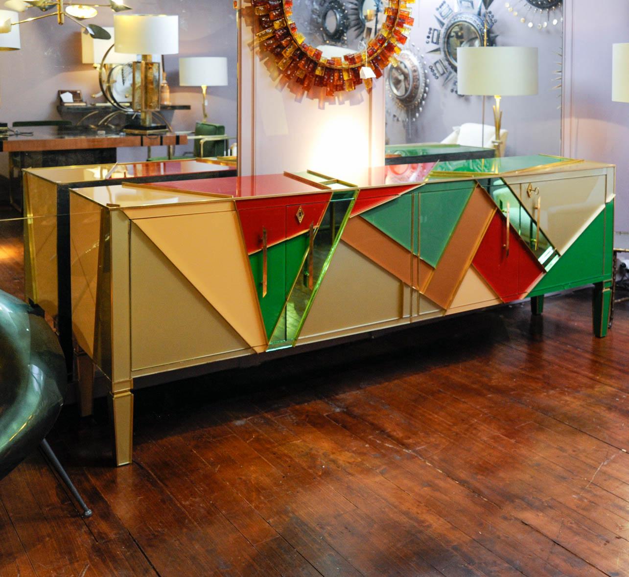 This long buffet is a 1950s piece of furniture customized by the Studio Glustin with geometrical brass fillet forms filled with colored mirrors. Made with four doors, you will find shelves and drawers inside to organize it.