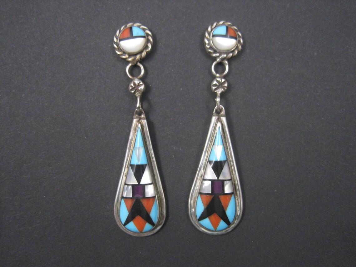 These gorgeous Southwestern earrings are sterling silver with coral, turquoise, jet, sugilite and mother of pearl inlay.

Measurements: 9/16 by 2 1/4 inches
Weight: 11.3 grams

Marks: Sterling, NA

Condition: Excellent

Earrings have been steam