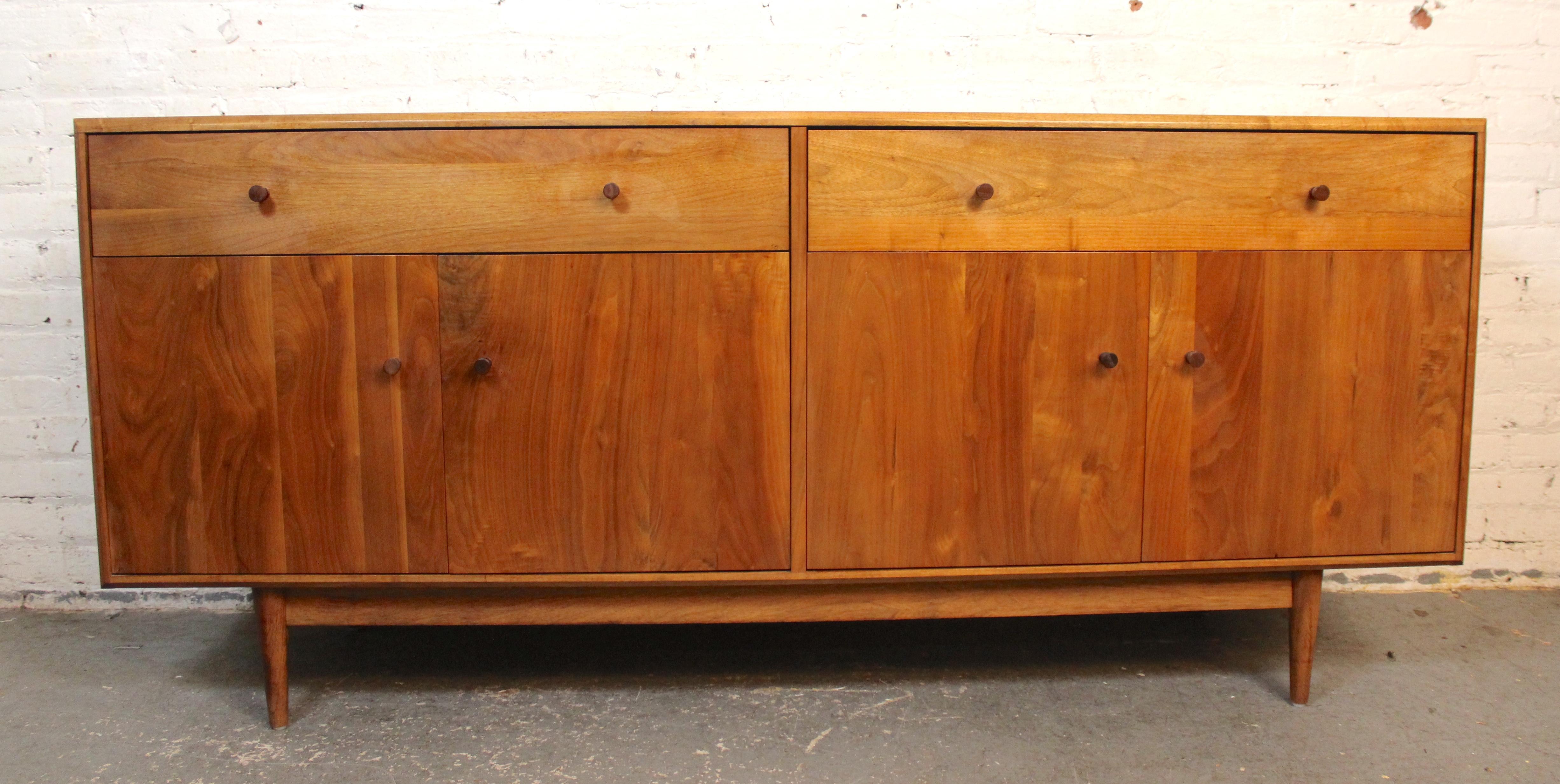 This long sideboard made of walnut wood grain features two cabinets concealed by four doors, and two wide drawers on top. Each is accented by a dark wood pull that plays off the light walnut finish. Cut outs in the back make it easy to store your
