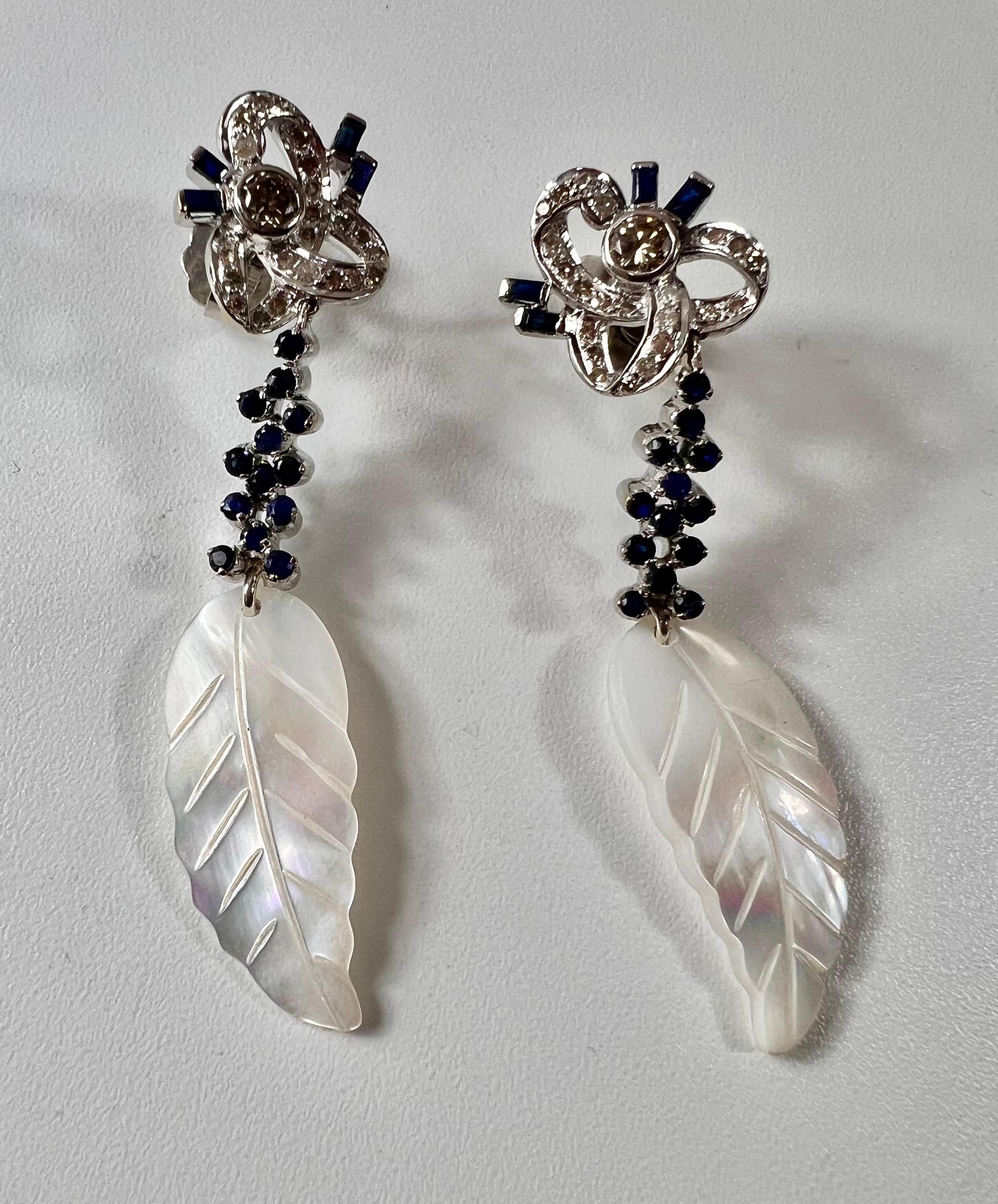 Long white gold earrings with a clean diamond, brilliant cut in chaton on openwork lacing in a row of diamonds and articulated cascade pendant of sapphires in claws
and mother of pearl feather 
Weight  9 grams
Length 32mm
2 bts  0,40 ct aprox total