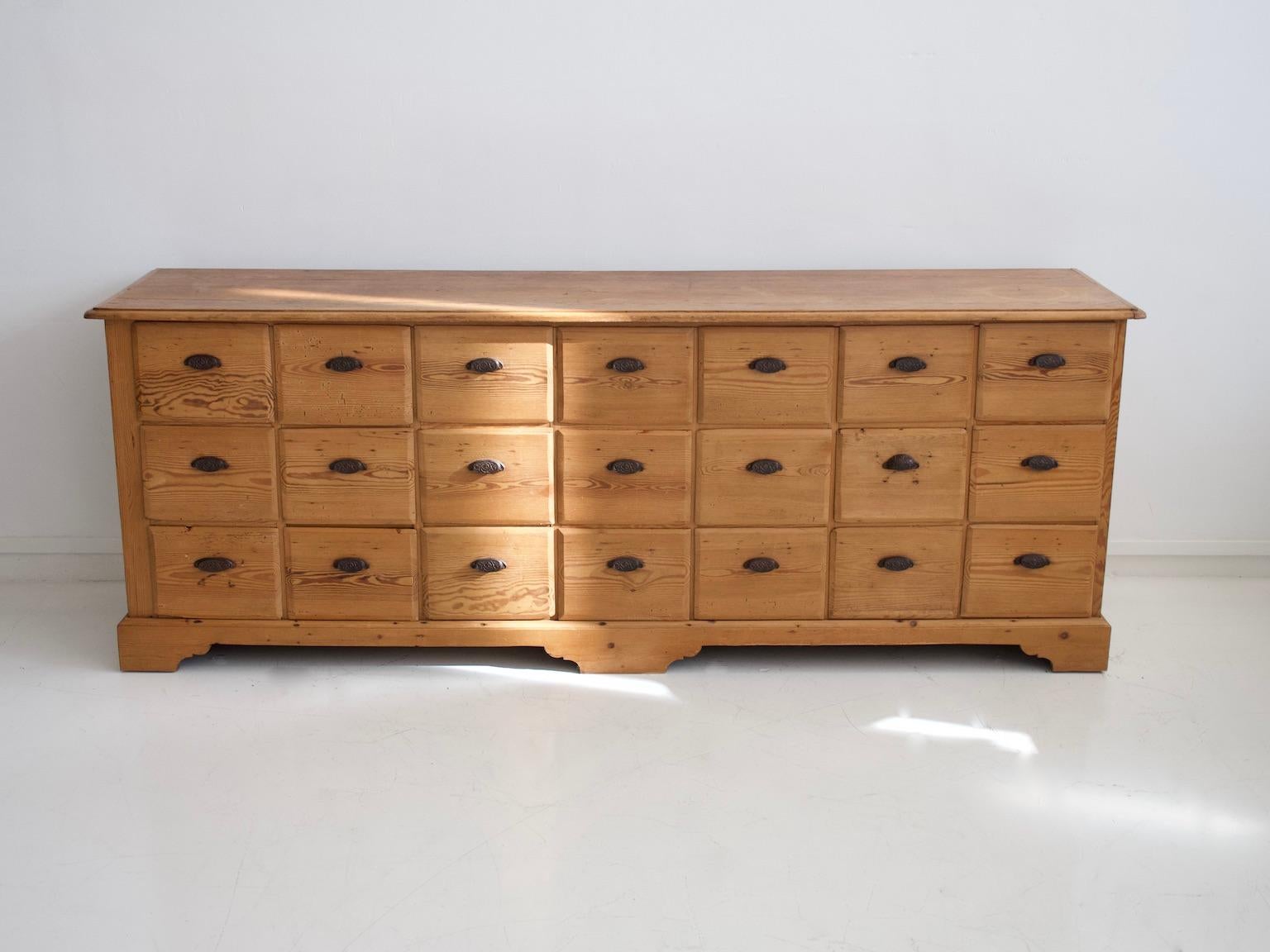 Large pine wood chest of drawers that could be used as a merchant desk. The chest features 21 drawers with metal handles. Made in the first half of the 20th century. Some age-related wear, marks and stains on top.