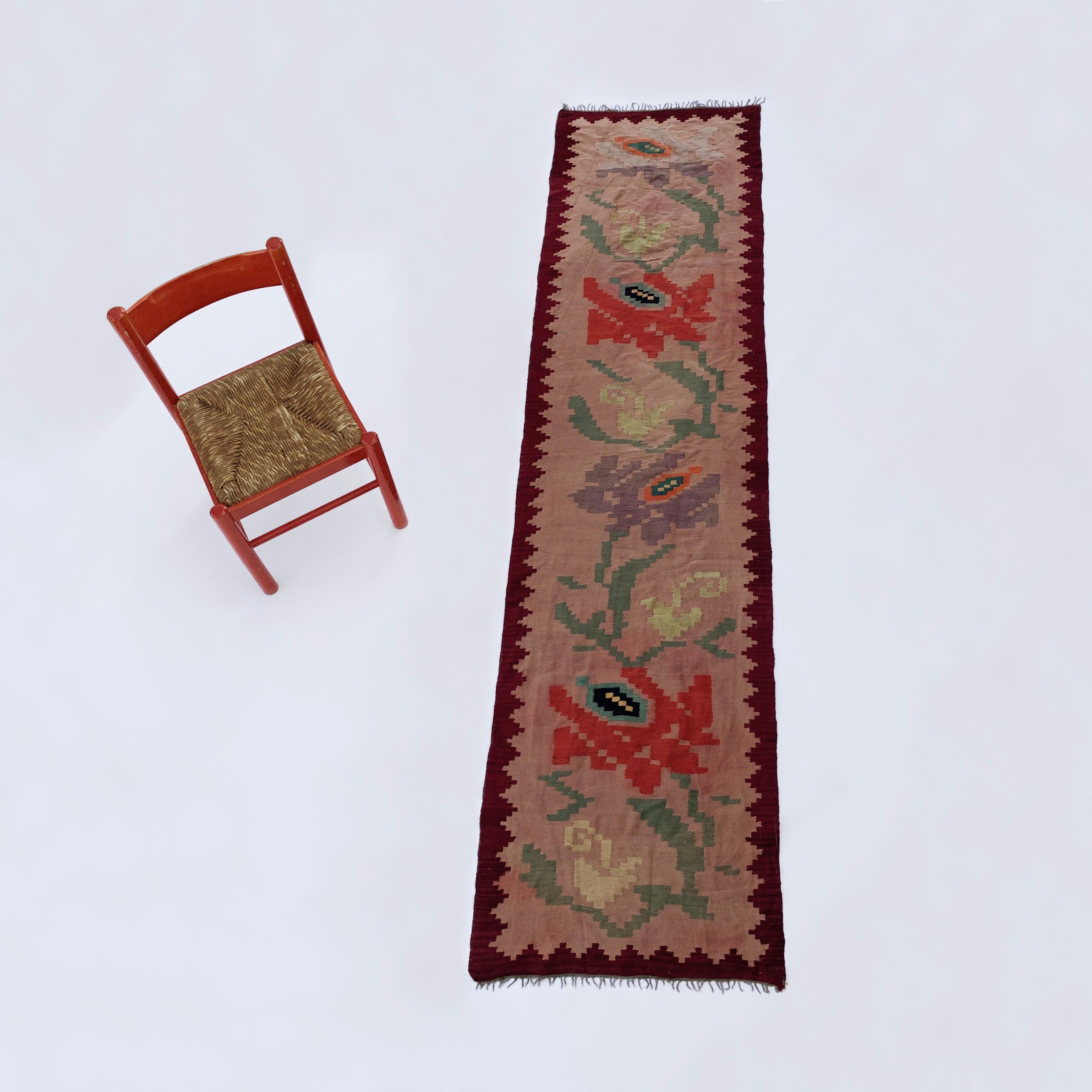 A stunning and lengthy wool runner from 1960s Greece, with an overall shade of pinky red. Can be used as a long runner in a corridor, as a throw over the back of a sofa, or even as a piece of wall art. The rose patterns are in red, purple, and