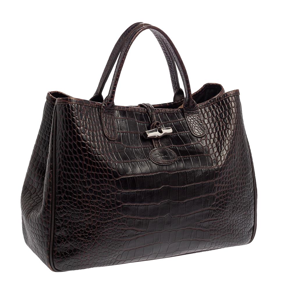 This Longchamp Roseau tote is perfect for daily use. Crafted from the finest leather and exhibiting a croc-embossed design, it has a luxe appearance. It has a brown shade and dual handles for comfortable handling. The bag has one main compartment to