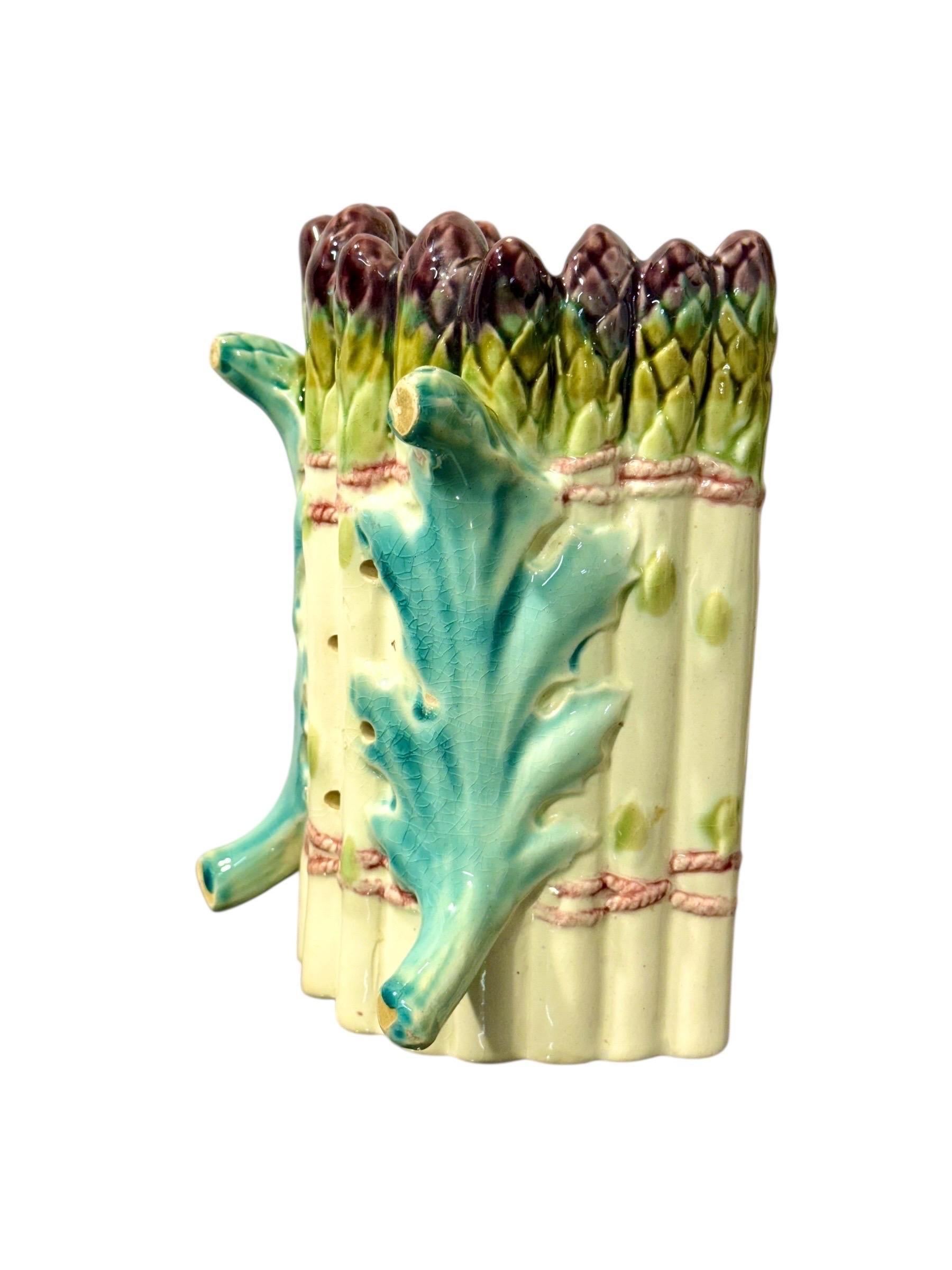 Cette ravissante assiette à asperges en majolique de Longchamp est un exemple classique de cette faïence française fantaisiste et très prisée des collectionneurs, produite à la fin du XIXe siècle. Réalisé en terre de fer richement émaillée,