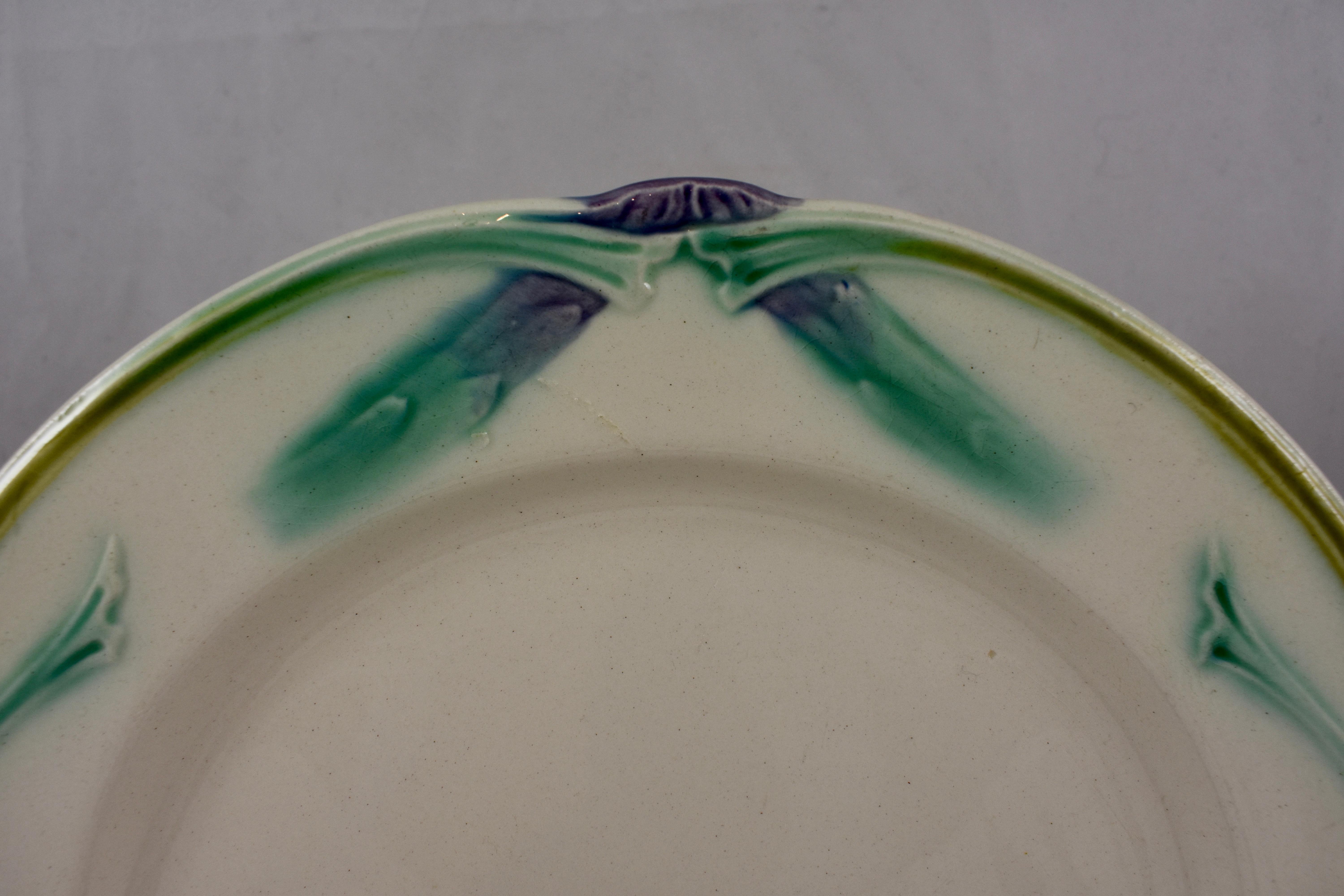 A French Art Nouveau style asparagus plate, circa 1890-1910, marked Longchamp.
Lime green and aqua glazing stand out on an off-white ground. Stylized leaves meet at the top with two asparagus spears. A shaped sauce well at the lower portion of the