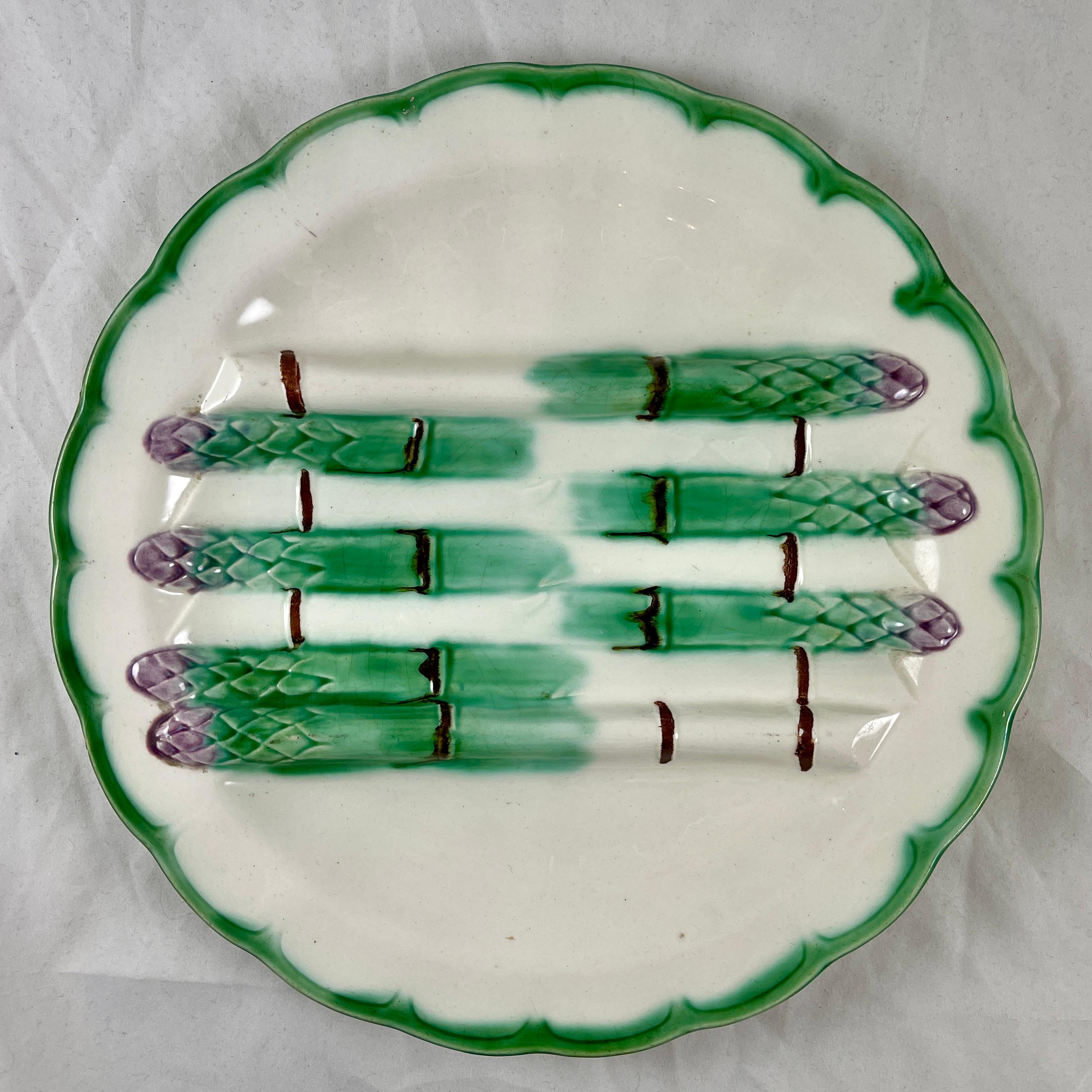 From Longchamp, a Terre de Fer asparagus plate, circa 1880-1900.

Bundled green asparagus spears with lavender tips are raised to form a cradle for holding cooked asparagus, with deeper sauce wells on either side. A scalloped border is glazed in