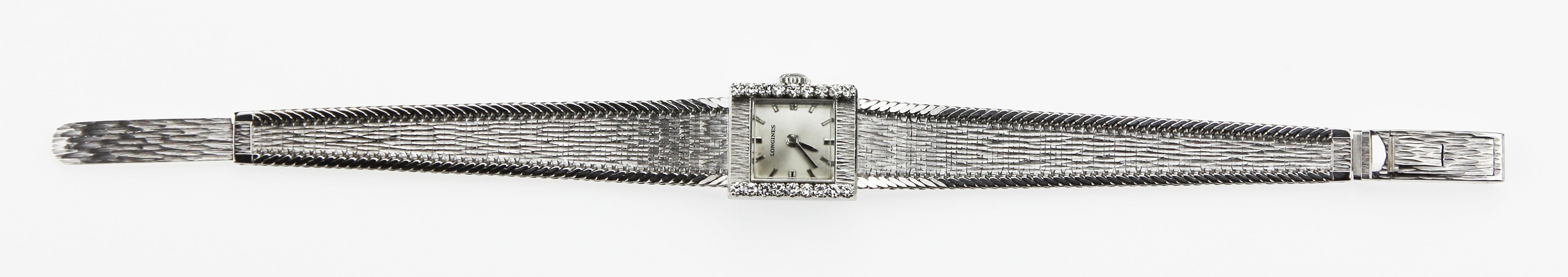 Longines 18 carat white gold watch with a simplistic square shaped face with a thick gorgeous gold textured border and two shoulder sides that are encrusted with diamonds. The wrist strap is an elegant thin flexible band with a gorgeous snake skin