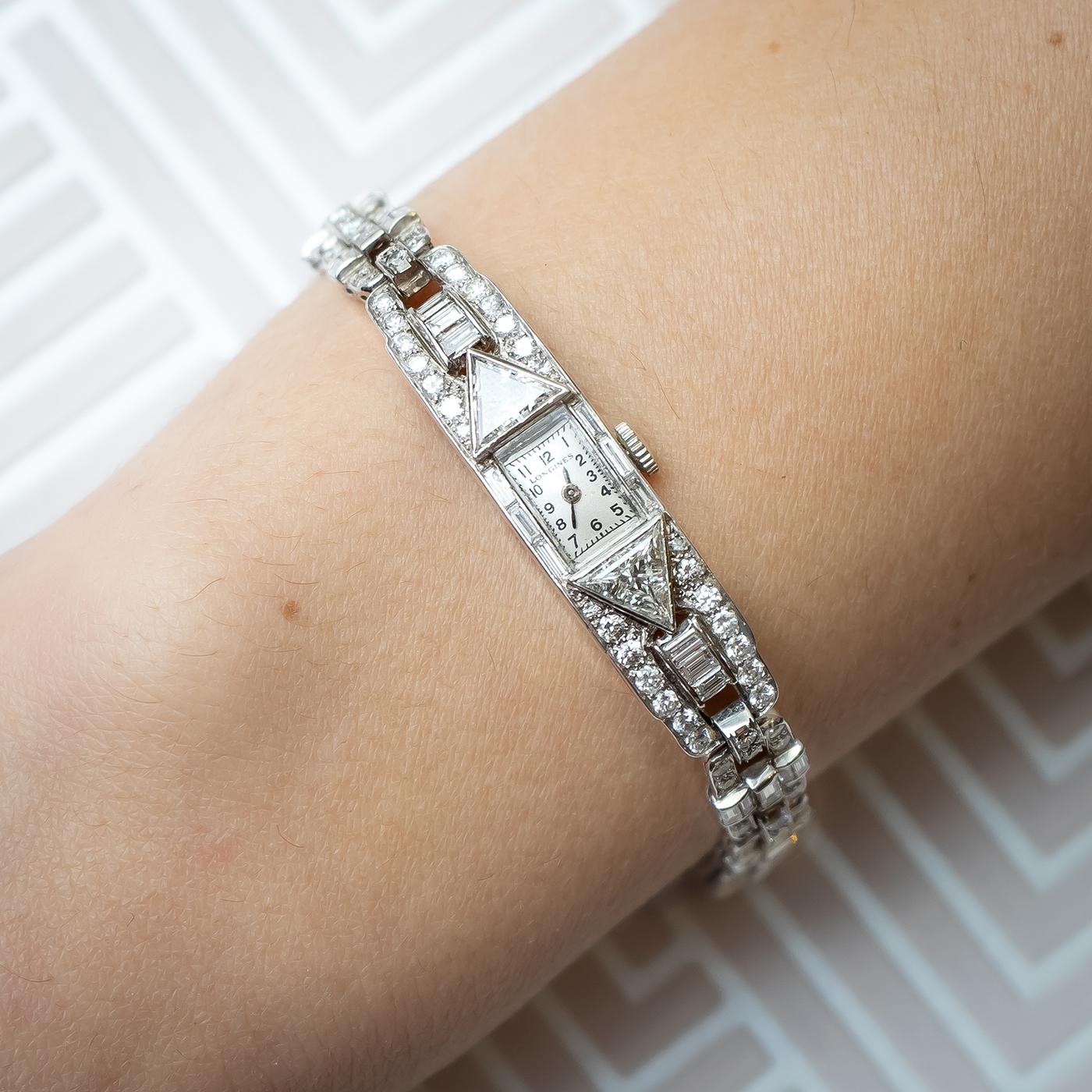 An Art Deco Tishman & Lipp Longines diamond cocktail watch, mounted in platinum, with a diamond set bracelet, with a rectangular, two piece hinged platinum case. It is attached to an open frame geometric link platinum bracelet, which measures