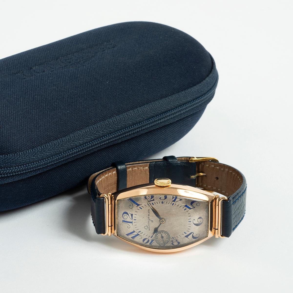 Our extremely rare Longines manually wound 14k yellow gold dress watch with integral lugs and tonneau case features an unusual dial in silver with sub seconds and art deco cursive hand applied numerals dial in blue. This vintage Longines is