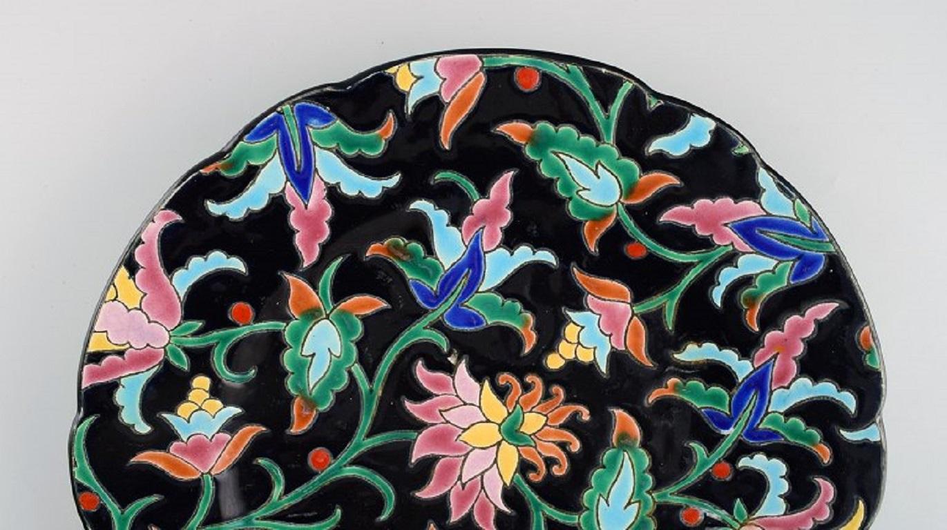 Longwy, France. Art Deco plate in glazed stoneware with hand-painted flowers and foliage on a black background. 1920s / 30s.
Diameter: 26 cm.
In excellent condition.
Stamped.

Emaux de Longwy was founded in 1798.
The French town of Longwy, in