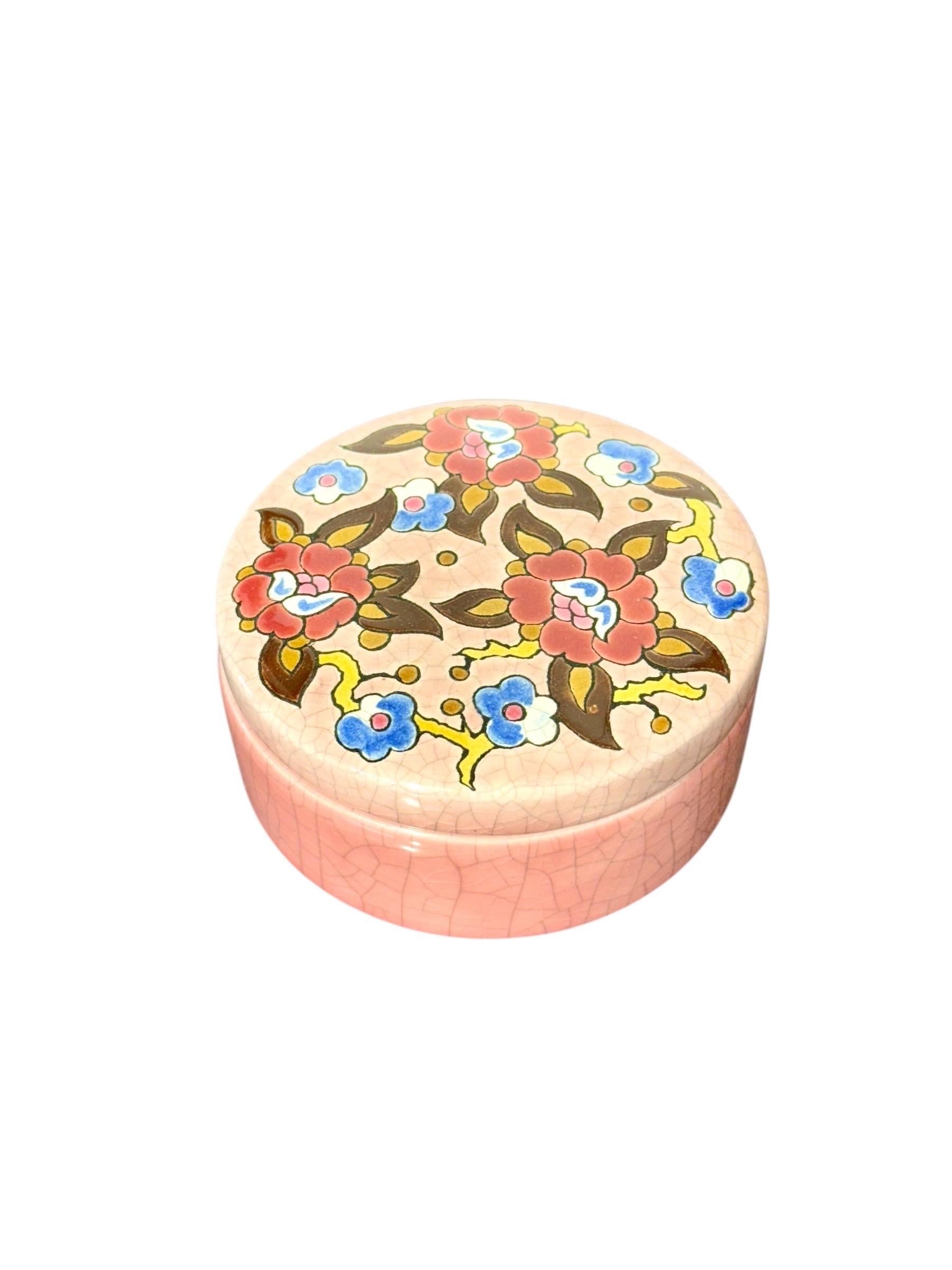 Questa graziosa scatola rotonda in ceramica della rinomata Faïencerie de Longwy è un bellissimo esempio del celebre artigianato decorativo della Maison. Caratterizzato dal caratteristico smalto crepla Longwy in un rosa tenue e romantico, il pezzo è