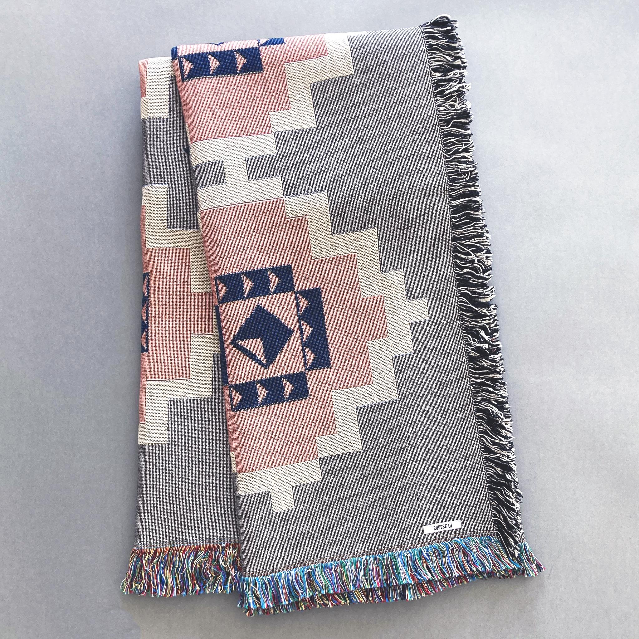 Gray geometric print woven throw with fringe edge, with accents of pink, white and navy. Woven with recycled cotton on a jacquard loom, made in the US. Each throw measures 54 x 72 inches.

This geometric patterned throw is inspired by early 20th