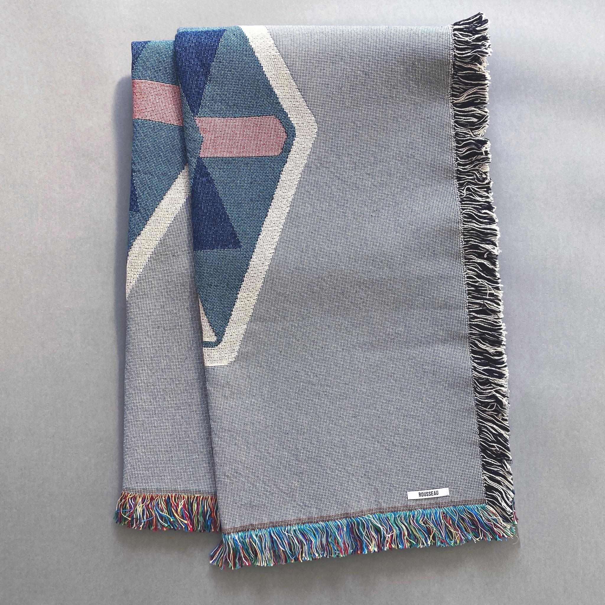 Nebelgraue gewebte Decke mit Fransenrand. Akzentfarben Ocker, Weiß, Rosa und Marineblau. Mit recycelter Baumwolle auf einem Jacquard-Webstuhl gewebt, hergestellt in den USA. Jede Decke ist 54 x 72 Zoll groß.

Die geometrisch gemusterte Decke ist von