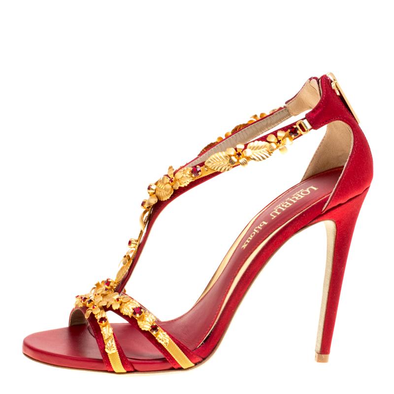 The intriguing gold-tone, floral embellishments that adorn the front straps and beautifully extend to the T-strap finishing just before the counters, make these red satin sandals from Loriblu Bijoux a statement piece worth-possessing. The pair has