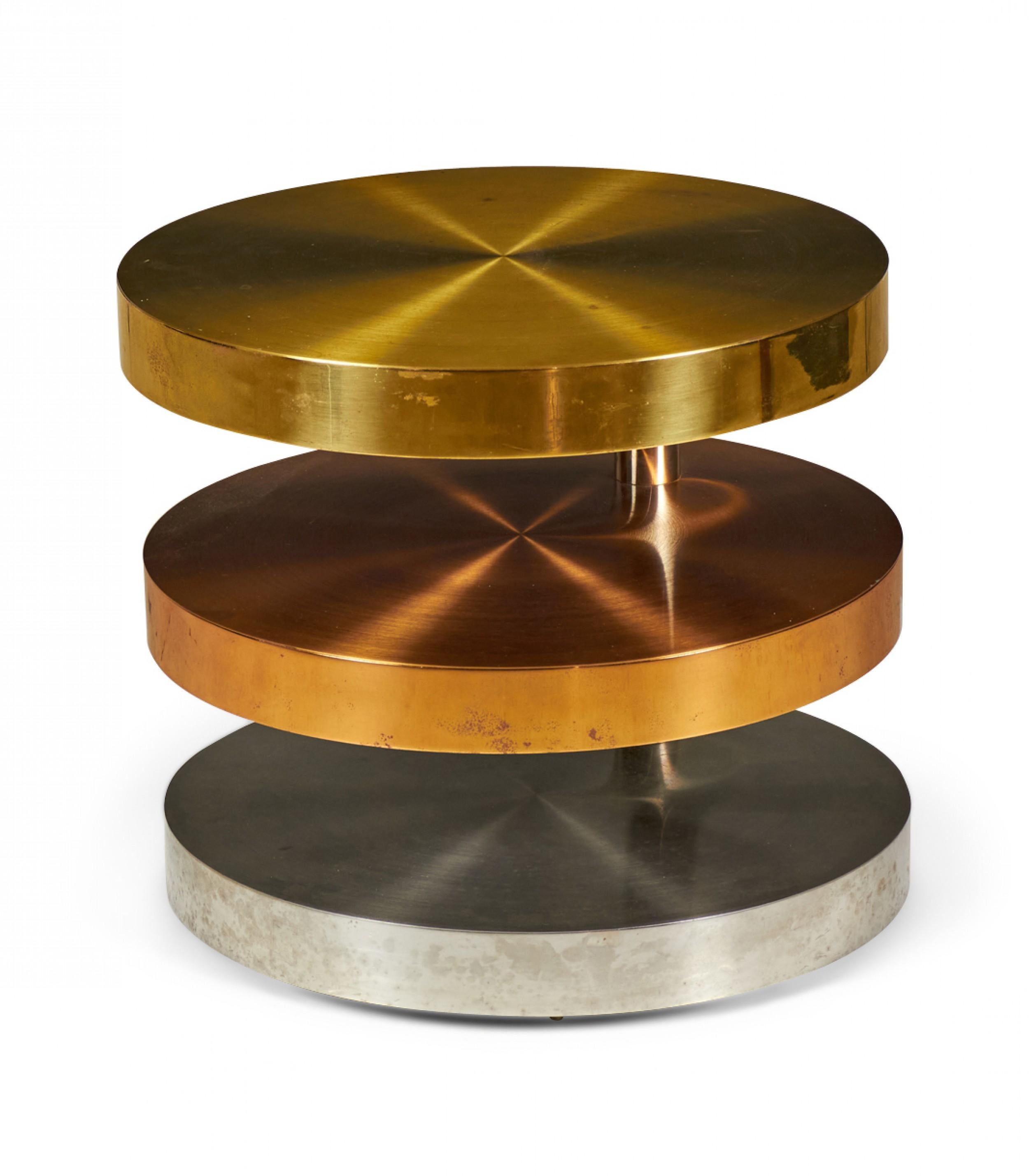 American High Style (circa 1980) coffee / cocktail table comprised of three swiveling circular tiers made from polished and satin brass, copper and chrome plated steel resting on rolling casters. (LORIN MARSH).
 
