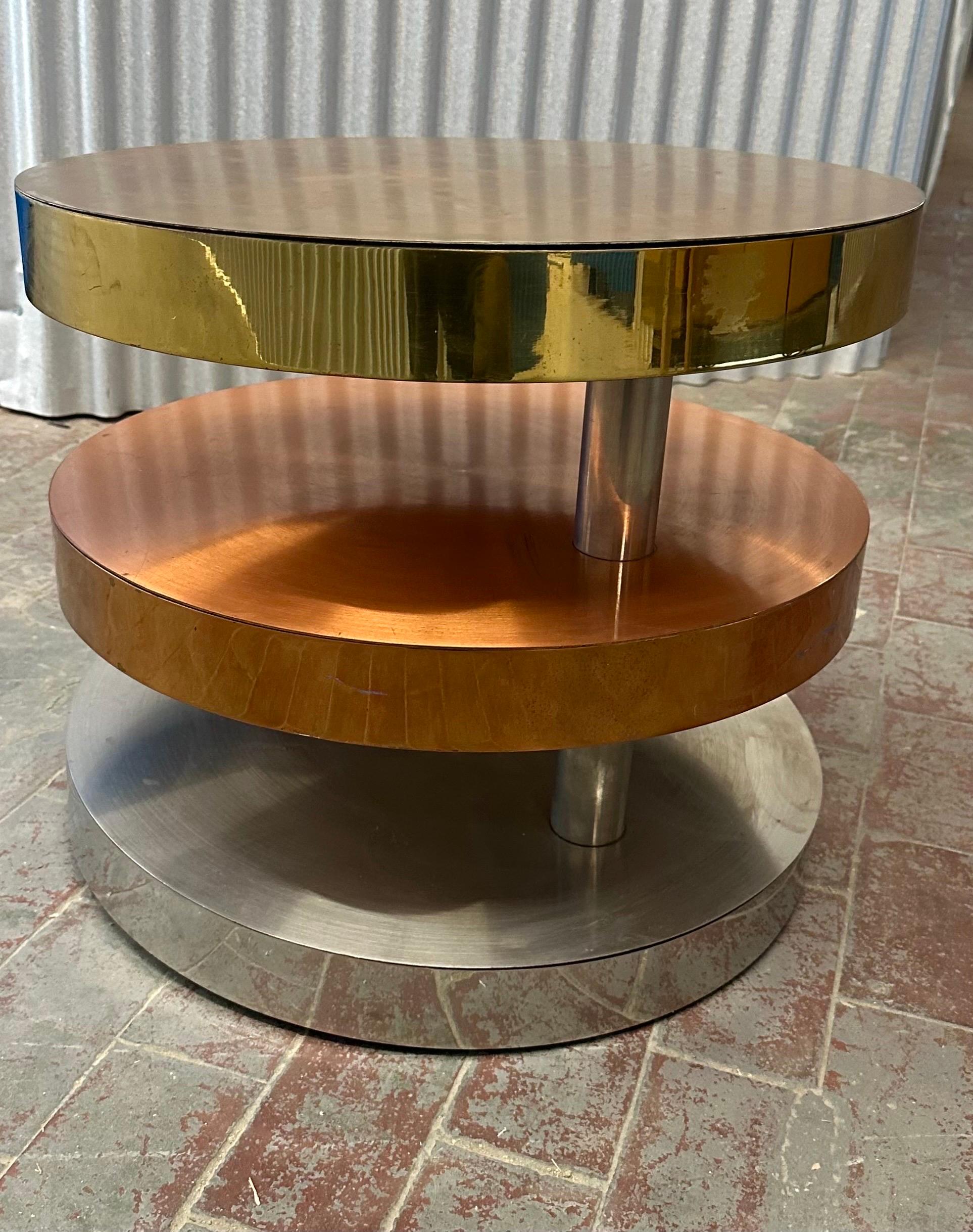 Comprised of three swiveling circular tiers made from polished and satin brass, copper and chrome plated steel resting on recessed rolling casters