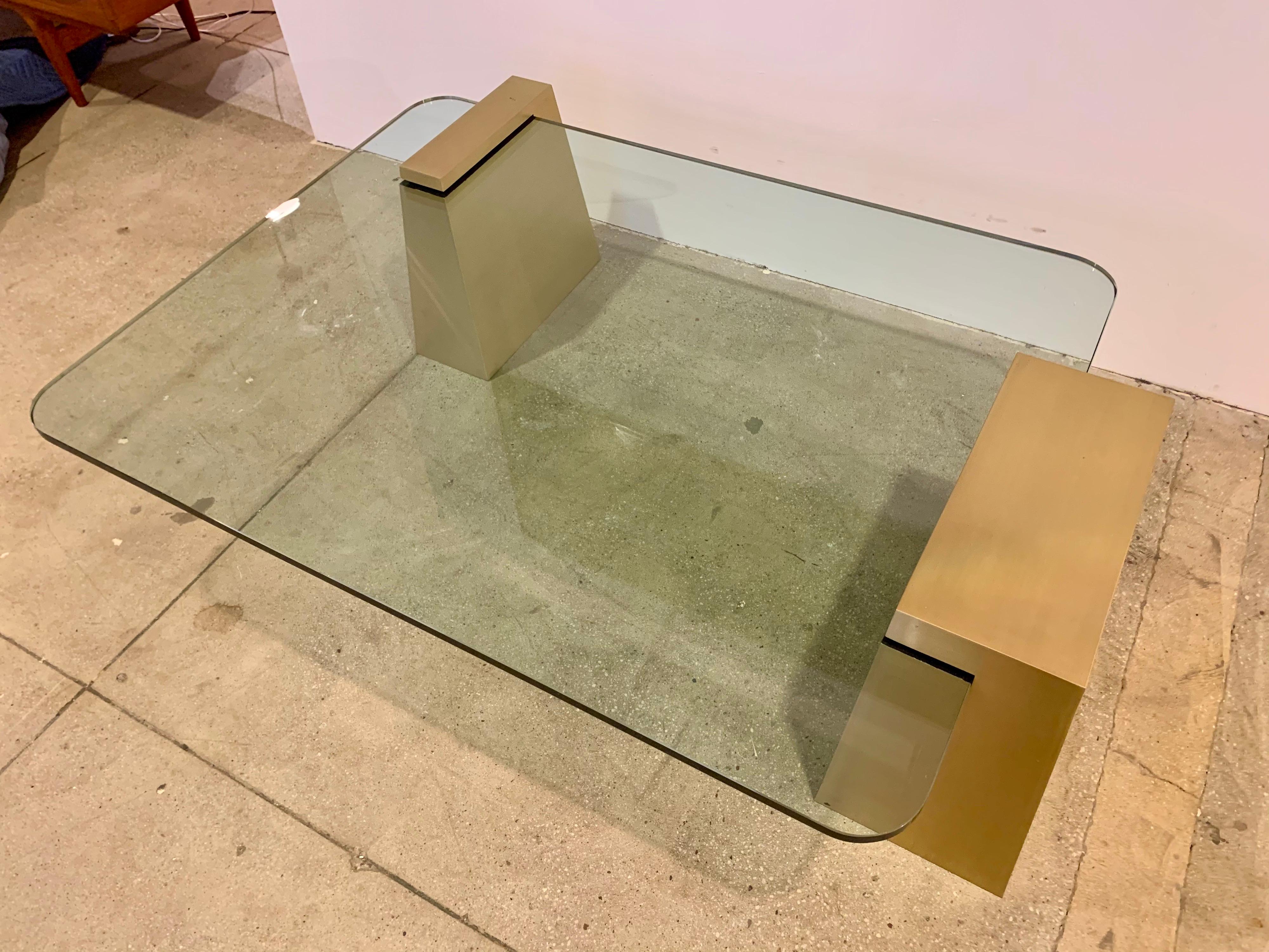 An original modern and sleek 1980s Lorin Marsh designed cocktail table composed of 1” thick rectangular glass top and aged satin brass bases. The bases can be arranged on different sides of the glass and can be used with different shaped glass.