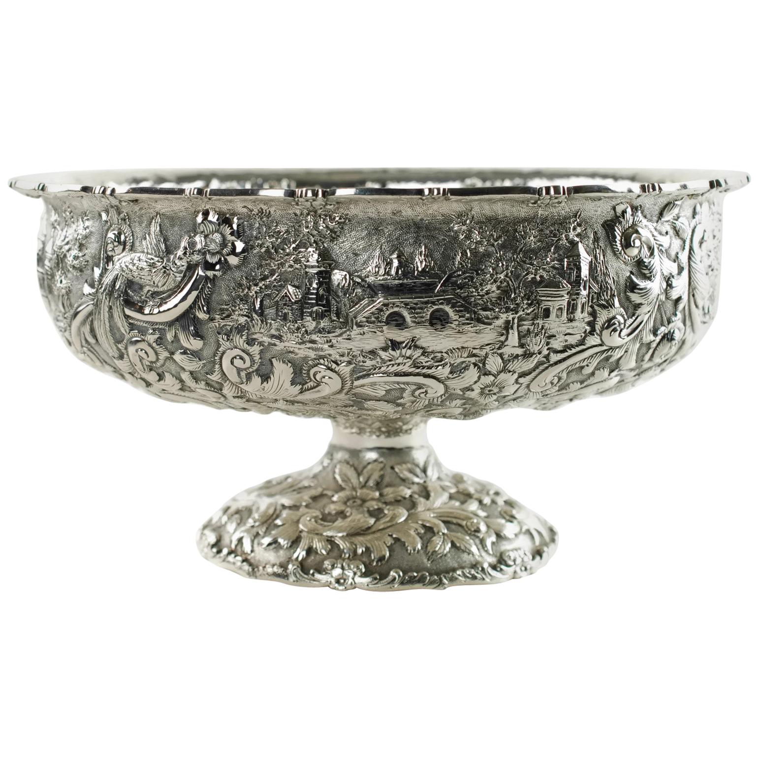 This large ornate early 20th century sterling silver centerpiece bowl has been made in the Castle pattern and is marked for The Loring Andrews Company of Cincinnati. The footed bowl features highly detailed all-over repoussé decoration which