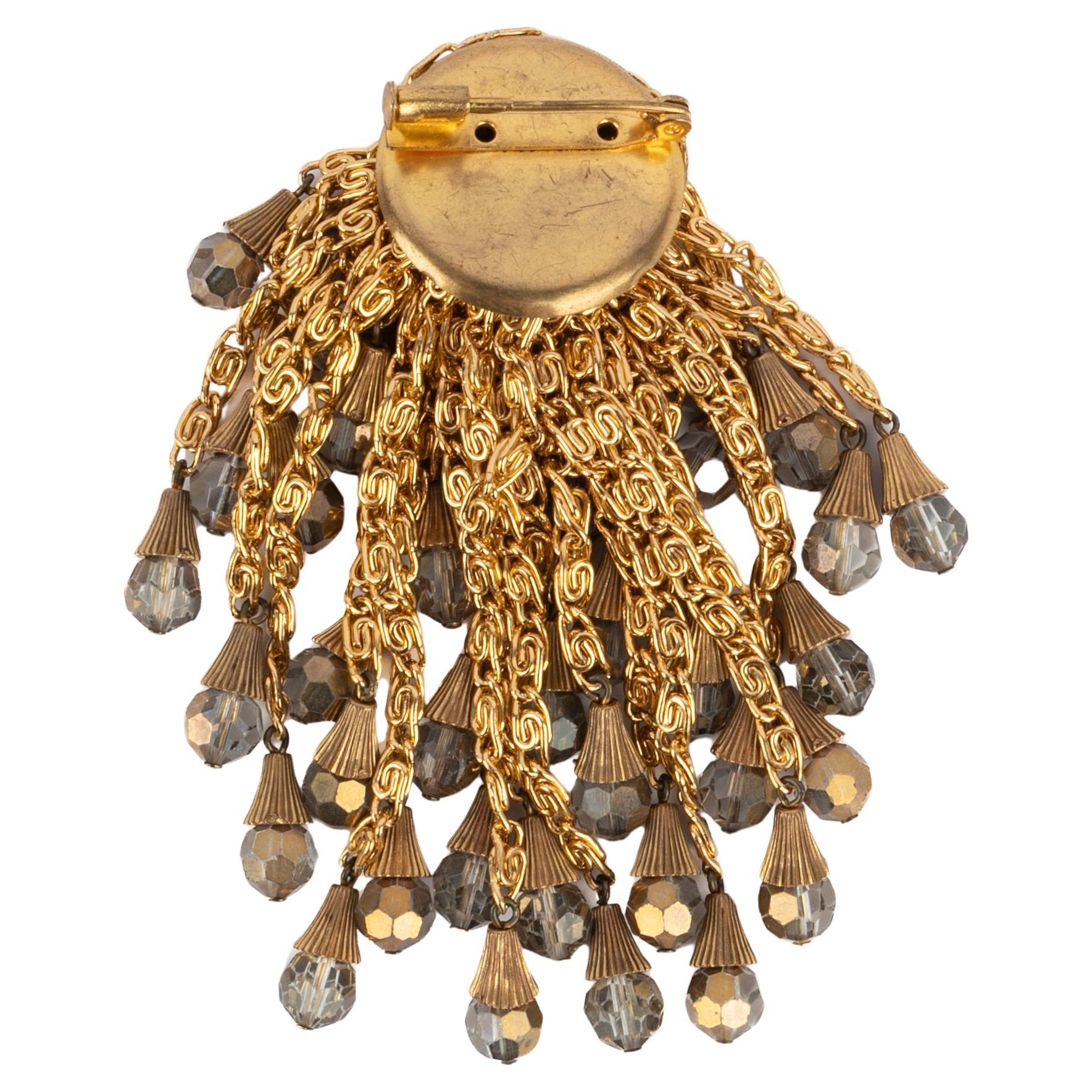 AZZARO - Goldene Metallbrosche mit einer für das Haus typischen Pomponkette aus Metall und Perlen.

Bedingung:
Sehr guter Zustand

Abmessungen:
Höhe: 9 cm

SKU:BR94


