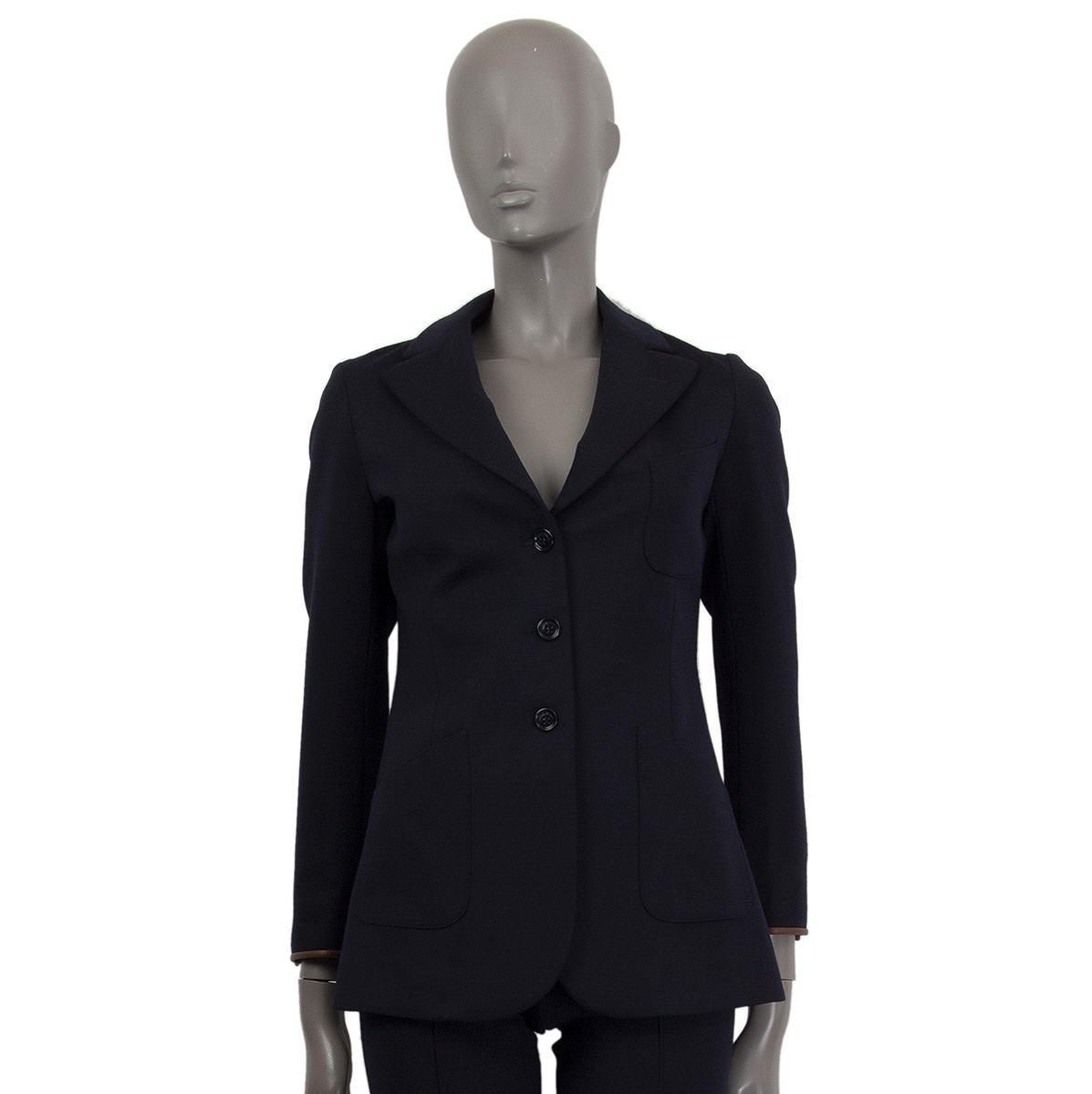 Loro Piana blazer in midnight blue virgin wool (88%), polyamide (10%) and elastan (2%) with brown leather hem. Three front pockets. Opens with three buttons on the front. Lined in navy blue and white and nude brown striped silk (100%). Has been worn